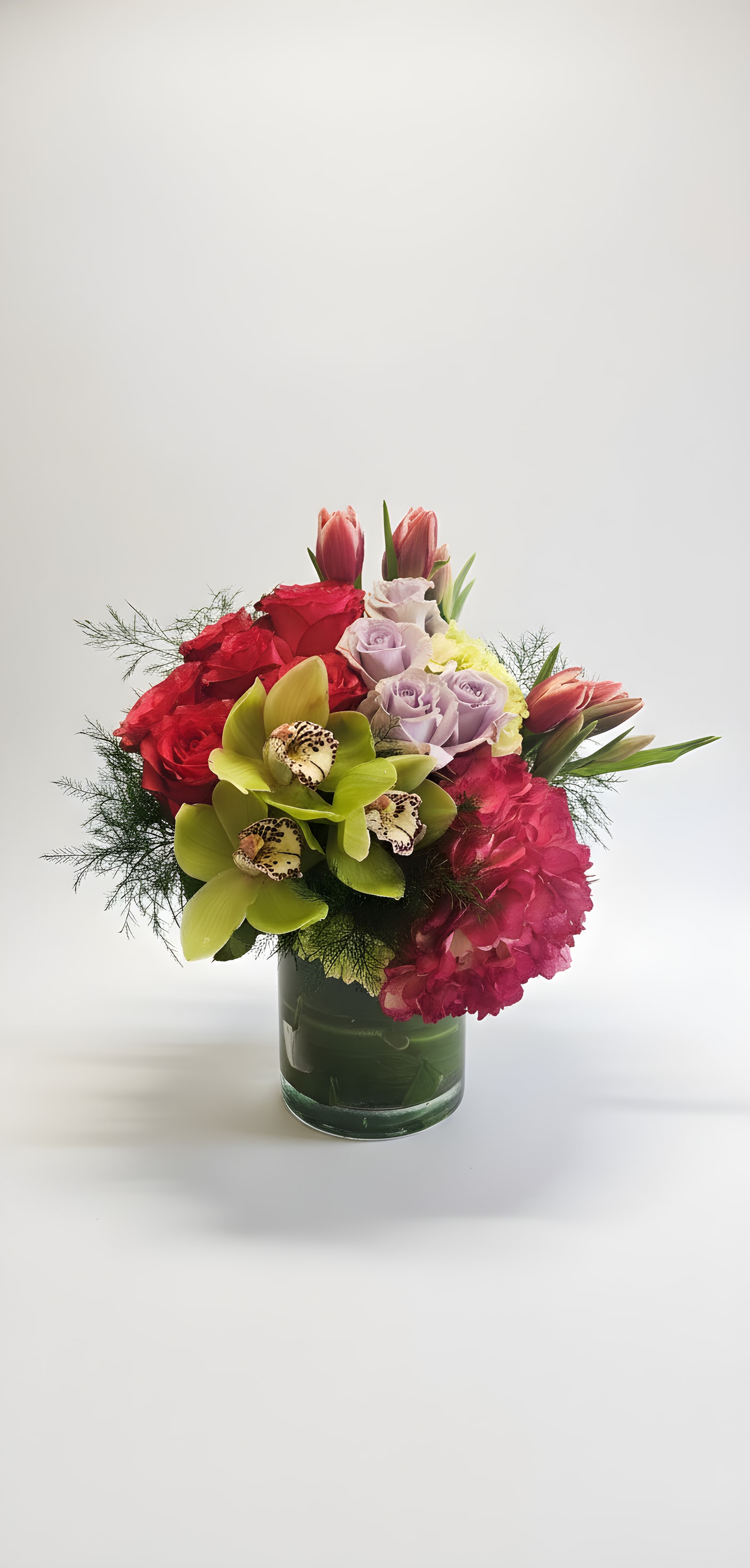 Mixed bouquet of roses, orchids, tulips, and hydrangeas in a glass vase