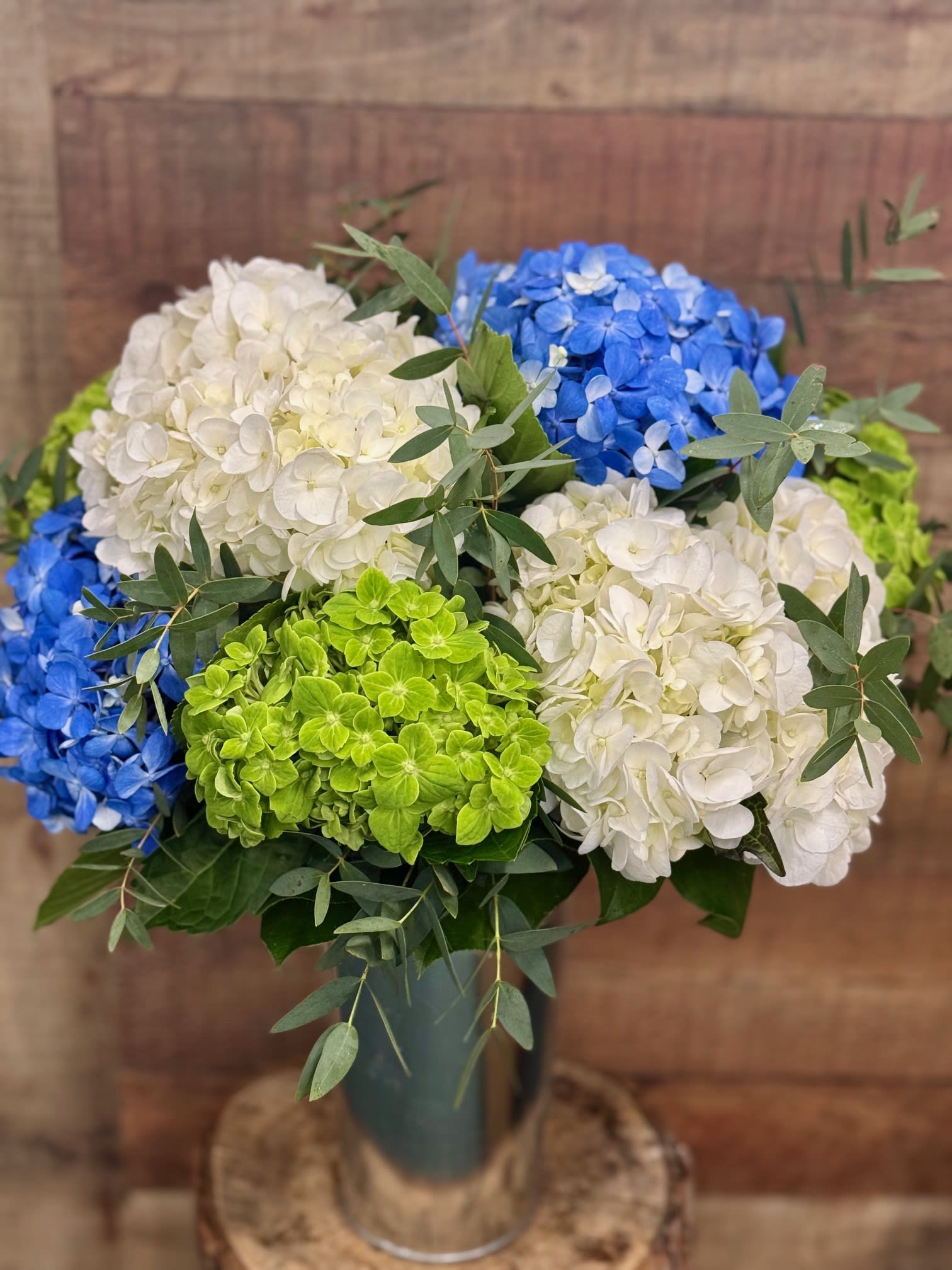 Blue, white, and green hydrangeas arranged in a tall glass vase