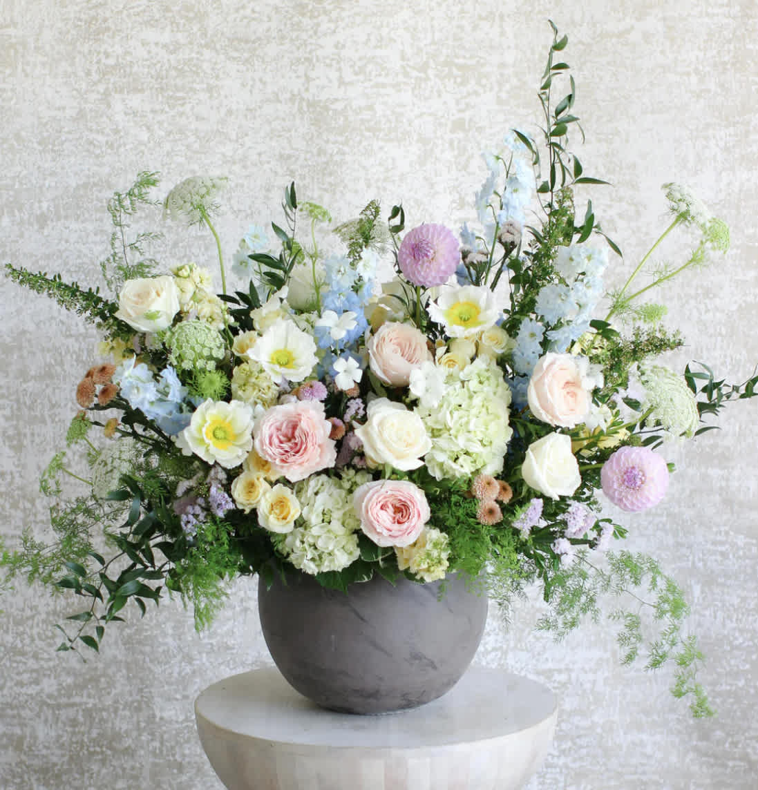 Large pastel arrangement of roses, hydrangeas and mixed blooms in a gray bowl vase on a pedestal table