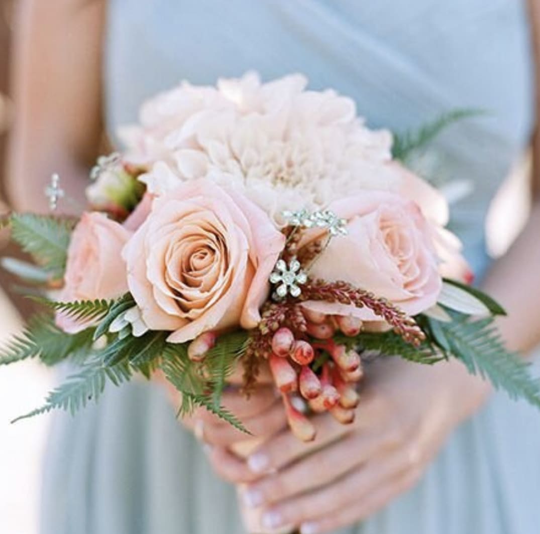 Hand-tied bouquet of peach roses and pale dahlias with berries held by a person in a light dress