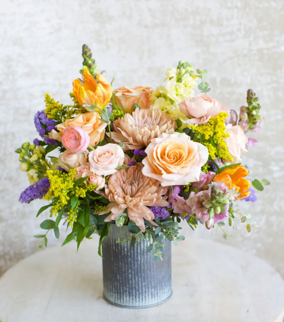 Peach and yellow mixed flower arrangement with roses and mums in a gray metal cylinder vase