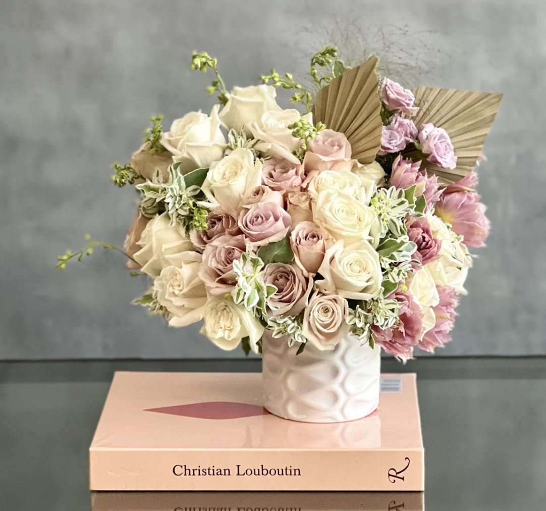 Pastel pink and cream rose arrangement with ruffled blooms in a white vase set on fashion books