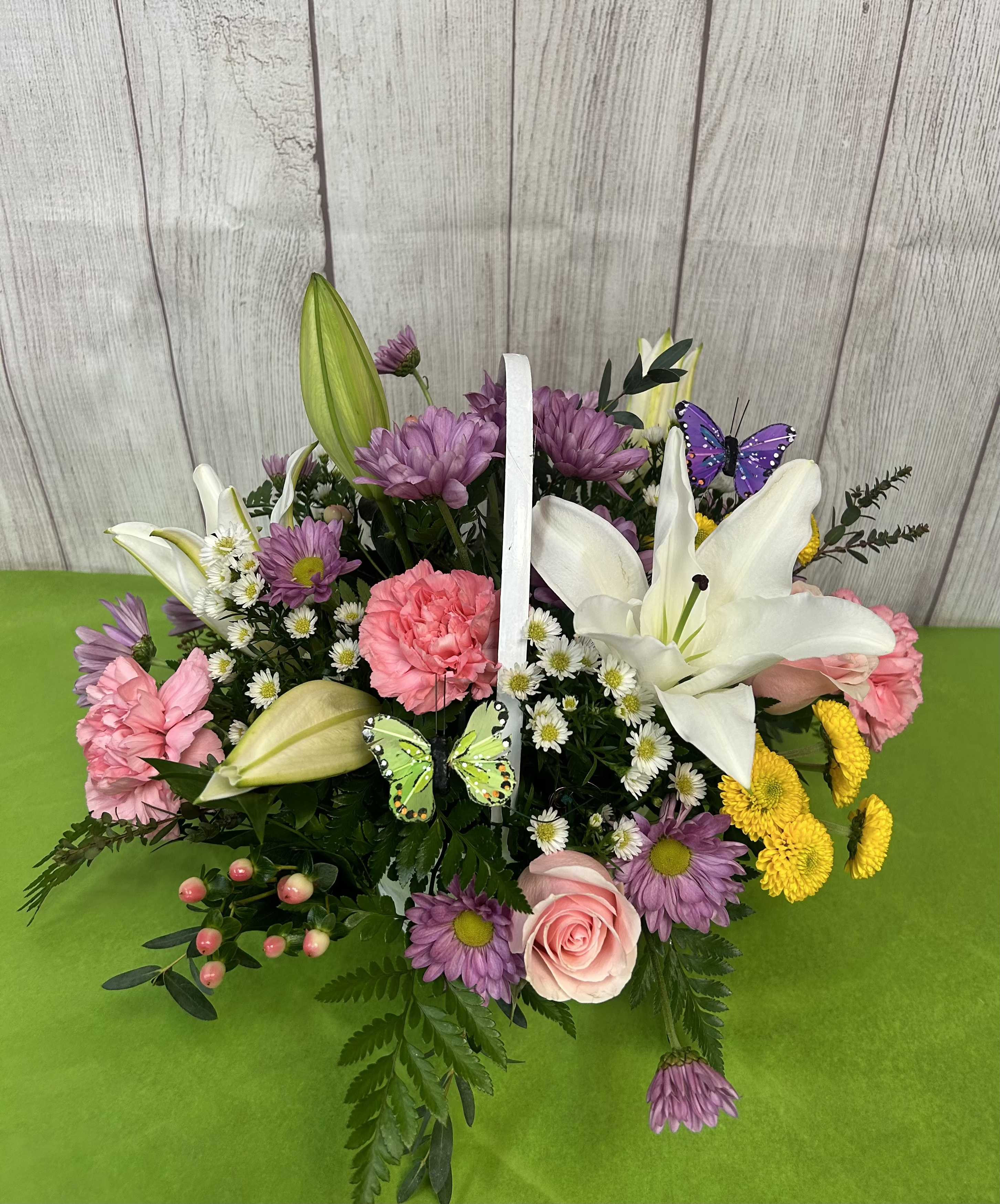 Basket arrangement with lilies, pink carnations, purple daisies, and butterflies