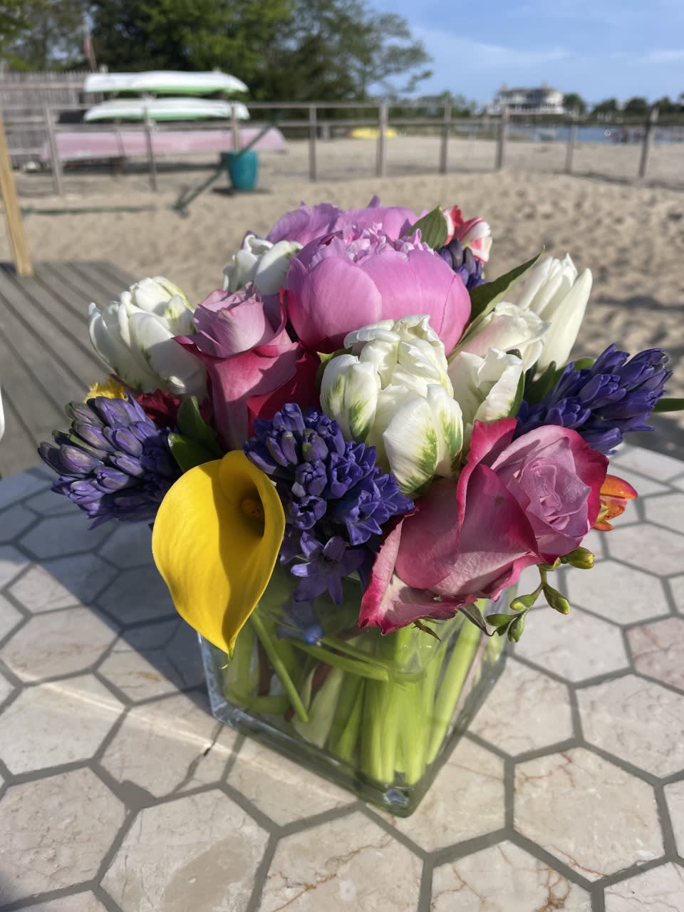 Mixed bouquet with pink roses, white tulips, purple hyacinths, and a yellow calla lily in a glass vase