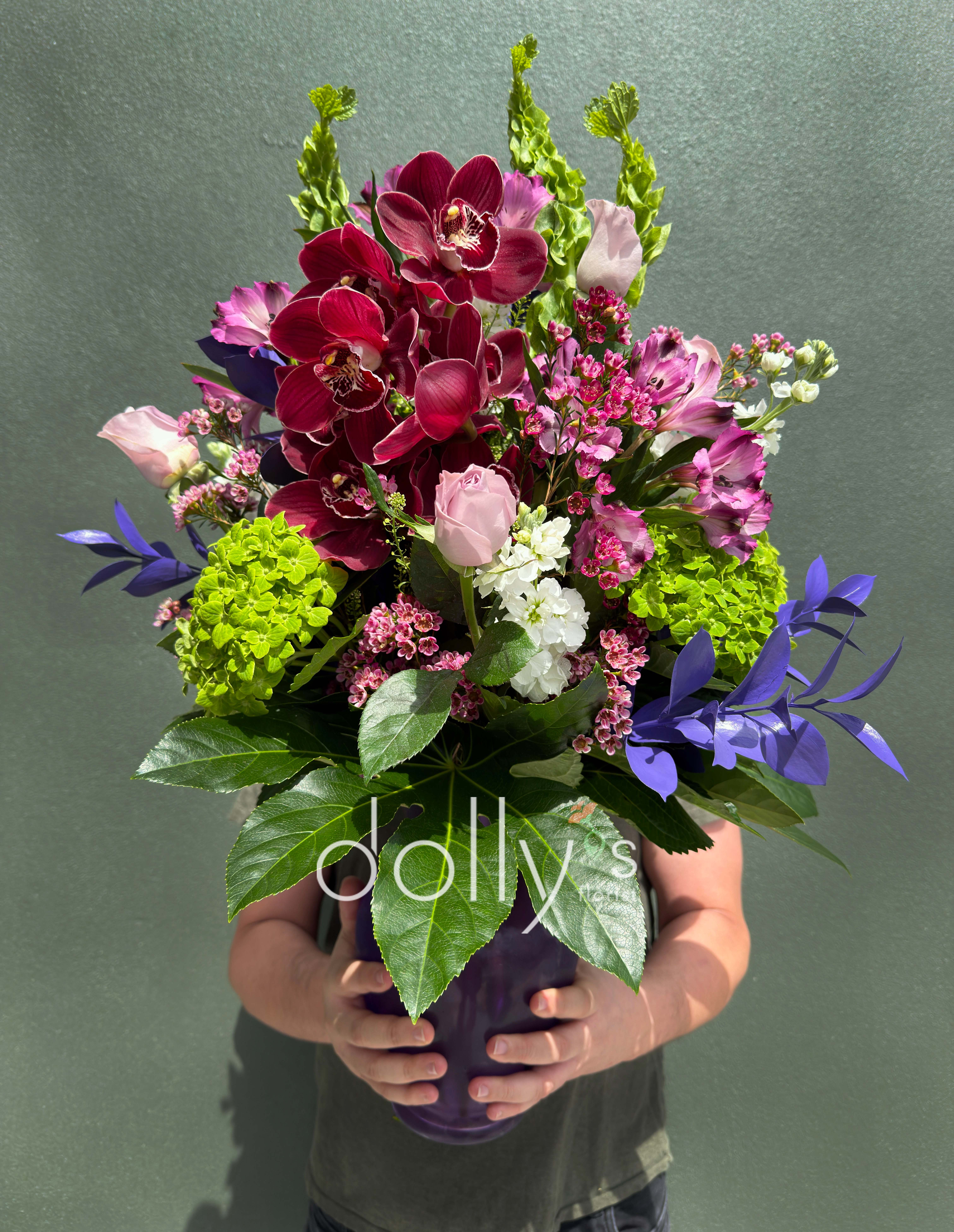Plum Serenade - Make a bold statement with the Plum Serenade, a masterpiece of texture and tone. We’ve curated a luxurious palette of deep wine-colored cymbidium orchids, vibrant alstroemeria, and premium pink roses to create a striking contrast against architectural Bells of Ireland. Arriving 'vase-ready' and overflowing with fresh greenery, this arrangement is the perfect centerpiece for the modern home or a distinguished office.