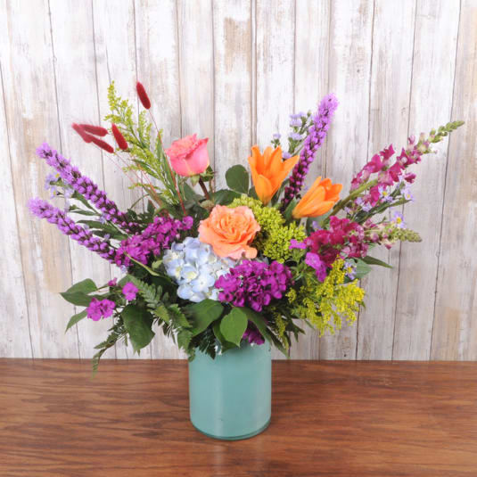 Garden Blend Turquoise - Bright, garden-fresh colors make this flower arrangement a joyful choice for birthdays, thank-you gifts, or just because - a vibrant flower arrangement that feels like a sunlit garden in bloom. The lively mix of roses and hydrangeas with snapdragons creates movement and height, so the person you're thinking of will feel celebrated the moment the box is opened.  This Garden Blend Turquoise features pink and peach roses paired with light blue hydrangea and orange tulip-like blooms, anchored by tall purple and magenta spires for an airy, asymmetrical silhouette. Bright yellow filler adds cheerful contrast, all arranged in a matte teal ceramic vase that complements the cool blue and turquoise tones while making the warm pinks and oranges pop. The overall composition is abundant but relaxed, giving a freshly picked look.  Perfect for sending warmth and appreciation to a friend, coworker, or loved one, this arrangement arrives ready to display in its ceramic vase. For best enjoyment, place in a cool spot out of direct sun and refresh the water every few days to keep the blooms bright and cheerful.