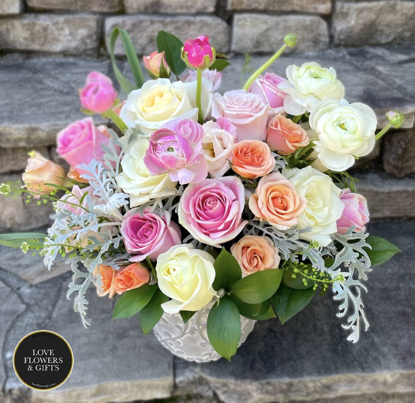 Pastel roses and ranunculus arranged in a white ceramic vase.