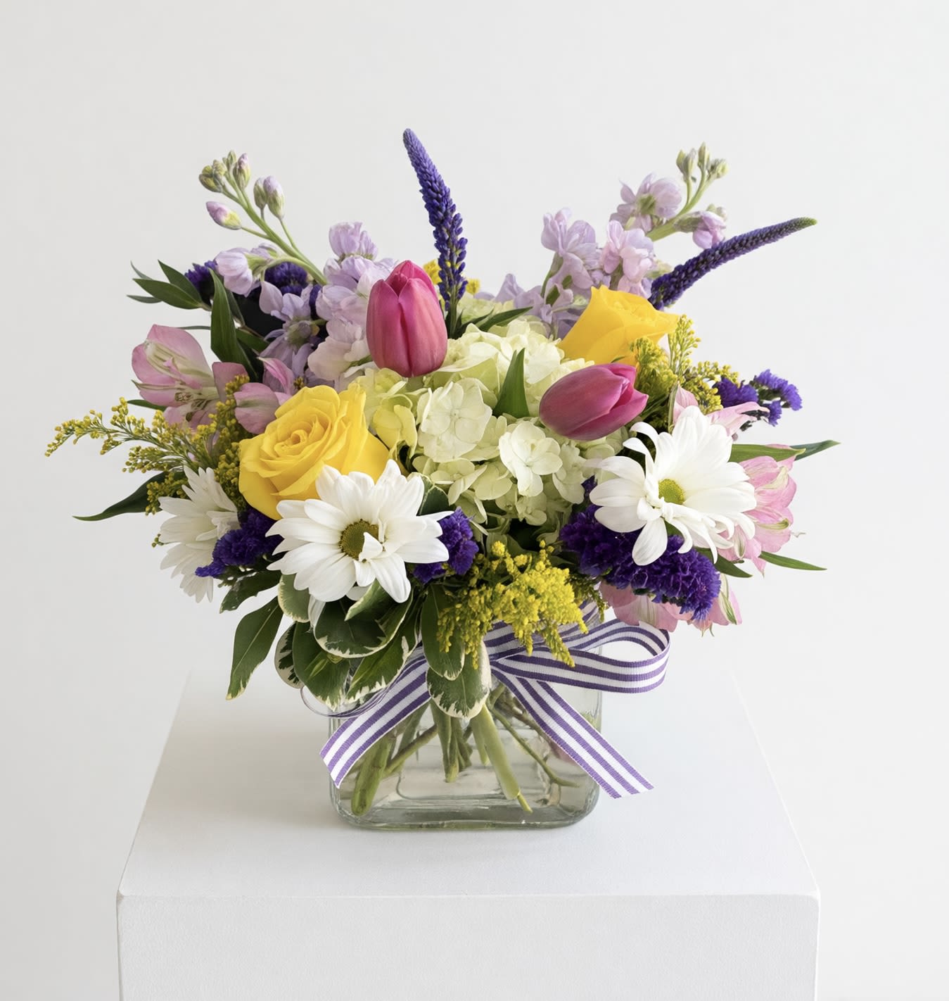 Spring Garden Cube  - A spring mix of fresh flowers in a clear cube vase. A mix of hydrangea, alstroemeria, roses, tulips, stock, daisies, Veronica and statice. All in shades of pink, yellow, lavender, purple and white. 