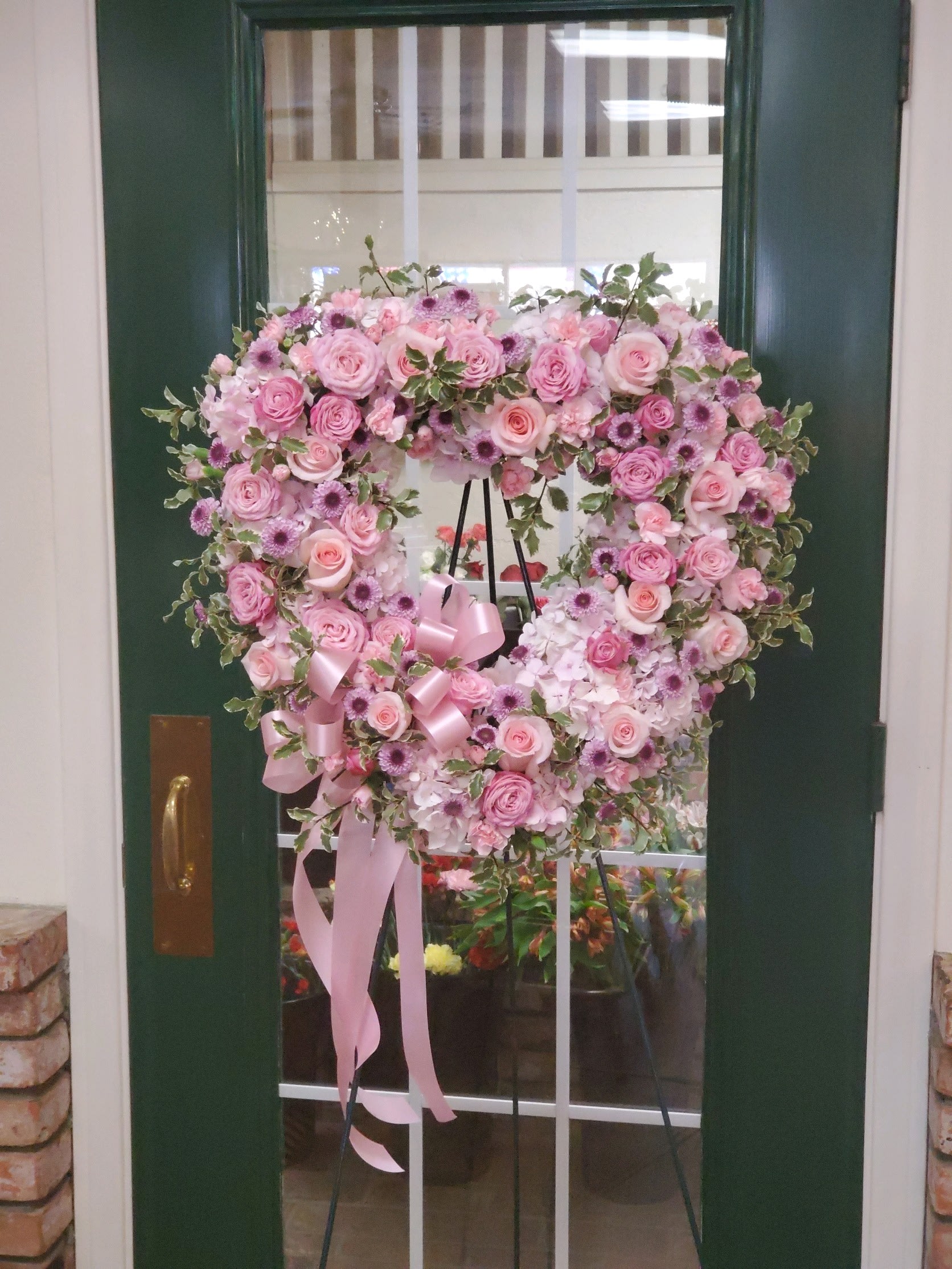 Heart-shaped pink floral wreath on a stand with ribbon