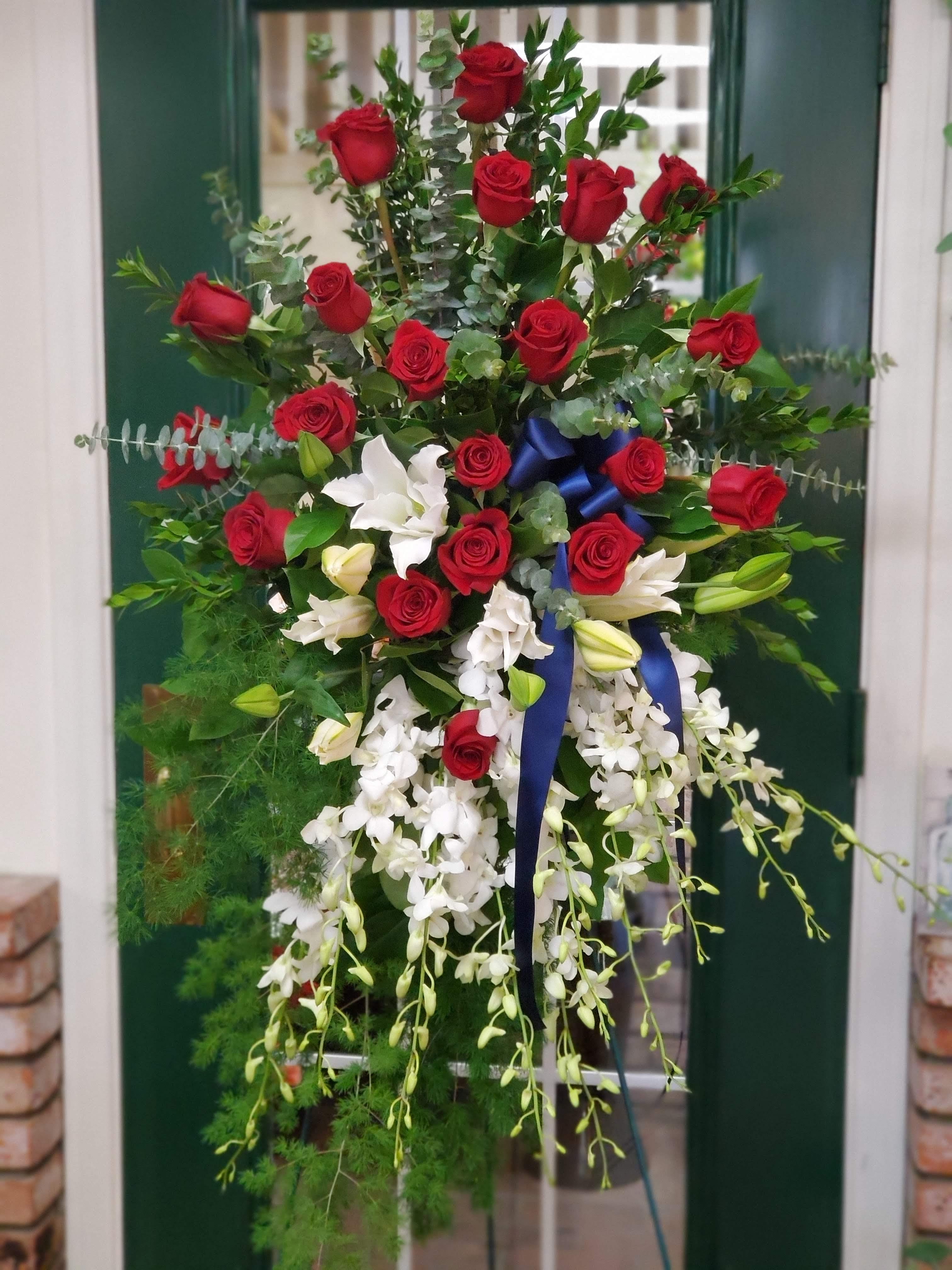Tall floral spray with red roses, white orchids, and a blue ribbon