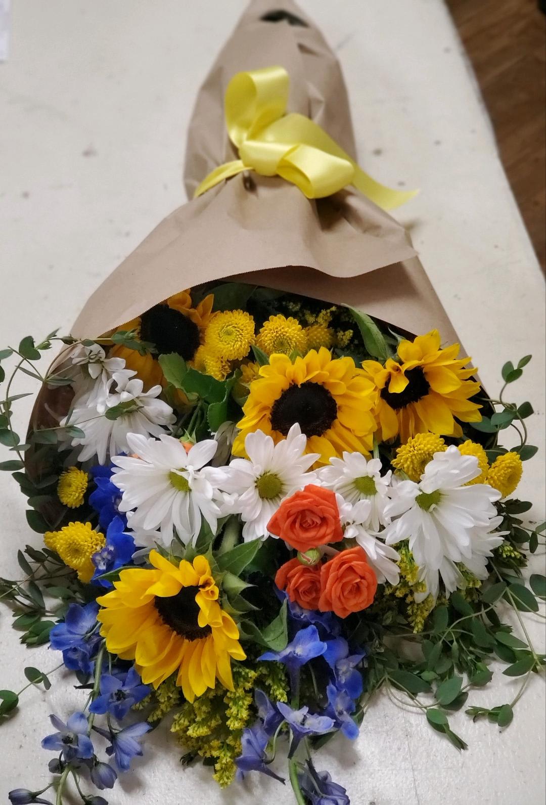 Bouquet of sunflowers, white daisies, and orange roses wrapped in brown paper