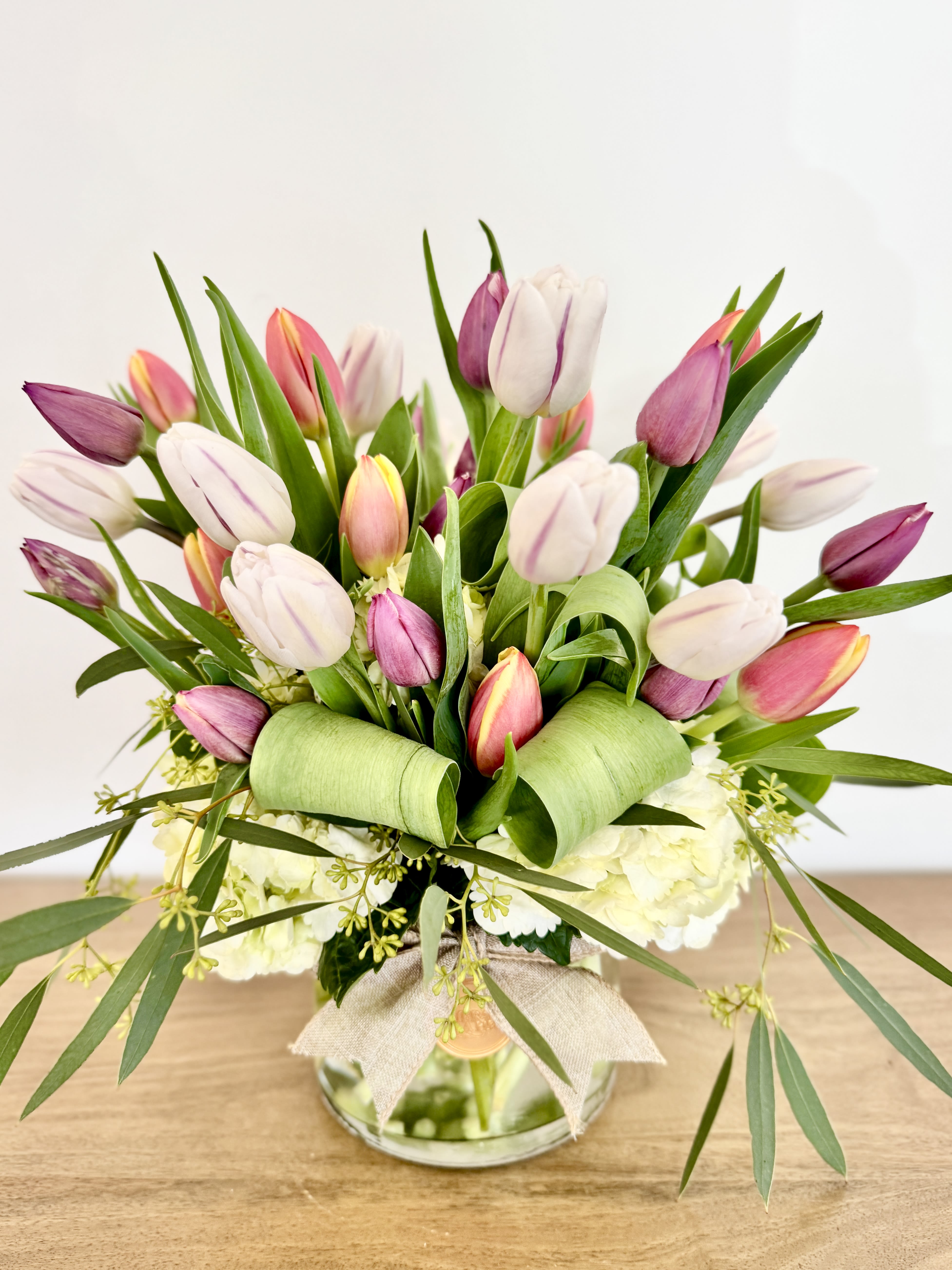 Pink and white tulips arranged in a glass vase with a burlap bow