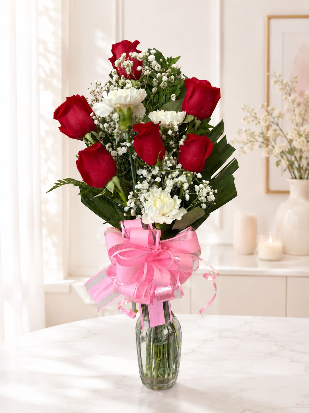 Red roses and white carnations in a glass vase with a pink ribbon