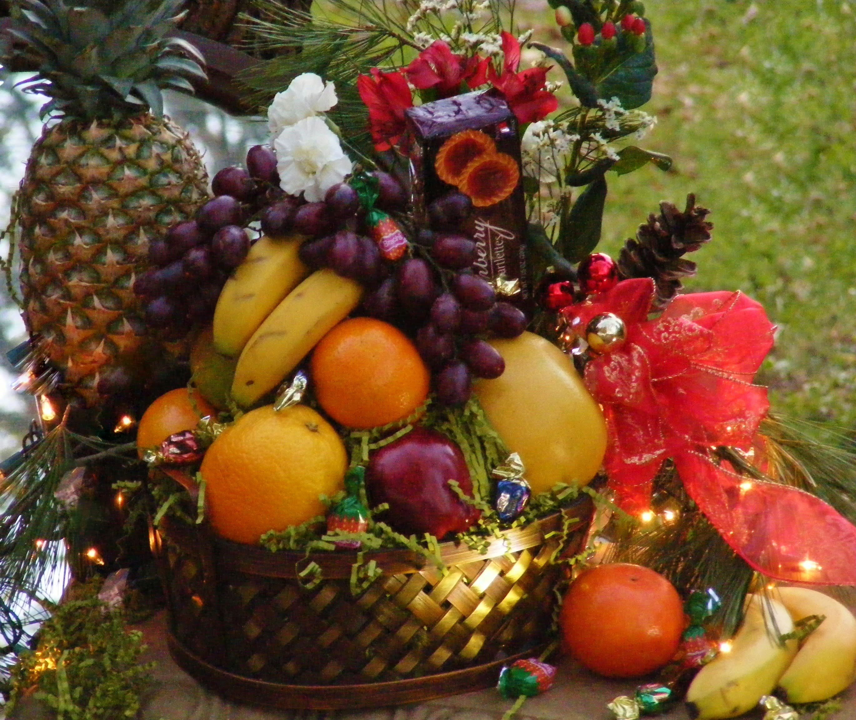 Fruit basket with pineapples, bananas, grapes, oranges, and a red bow