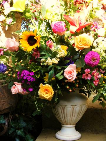 Mixed bouquet with roses, sunflowers, and lilies in a white urn vase