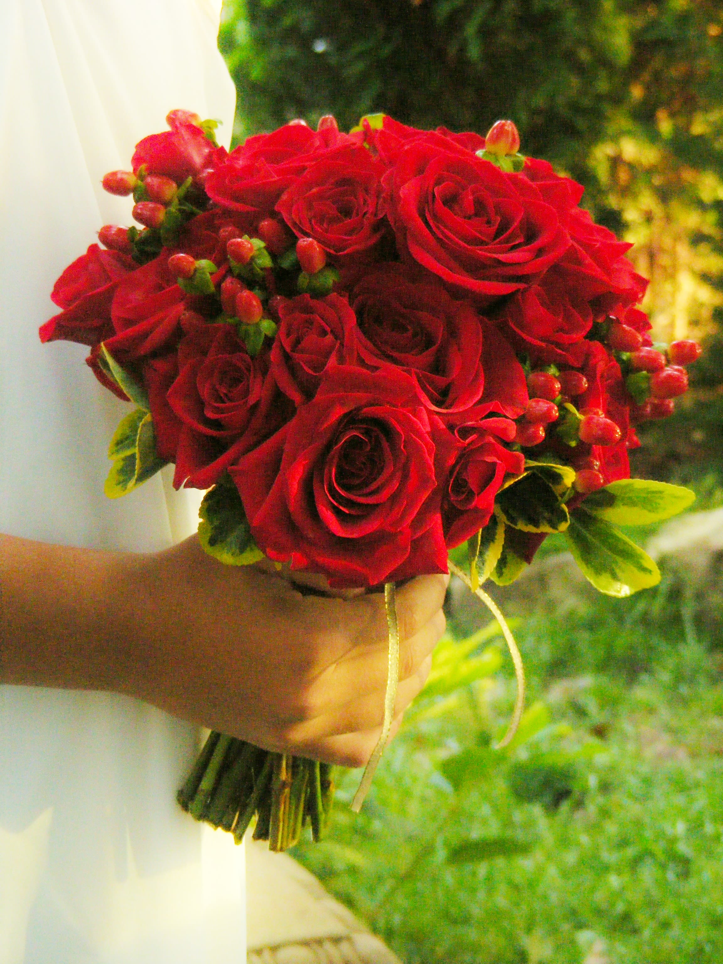 Handheld bouquet of red roses with small berry accents