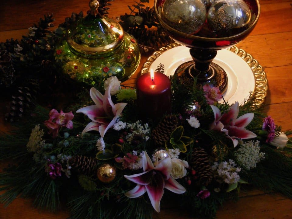Holiday centerpiece with lilies, a red candle, and decorative ornaments