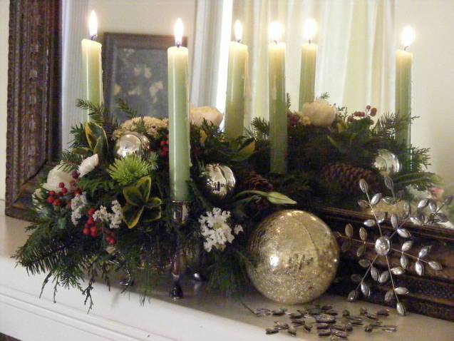 Holiday candle centerpiece with greenery and ornaments on a mantel
