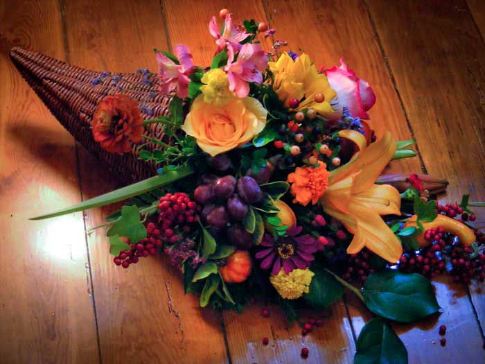 Cone-shaped floral arrangement with roses, lilies, and berries on a wooden floor