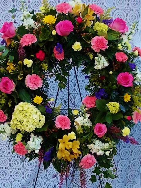 Large floral wreath on a stand with pink, yellow, white, and purple blooms