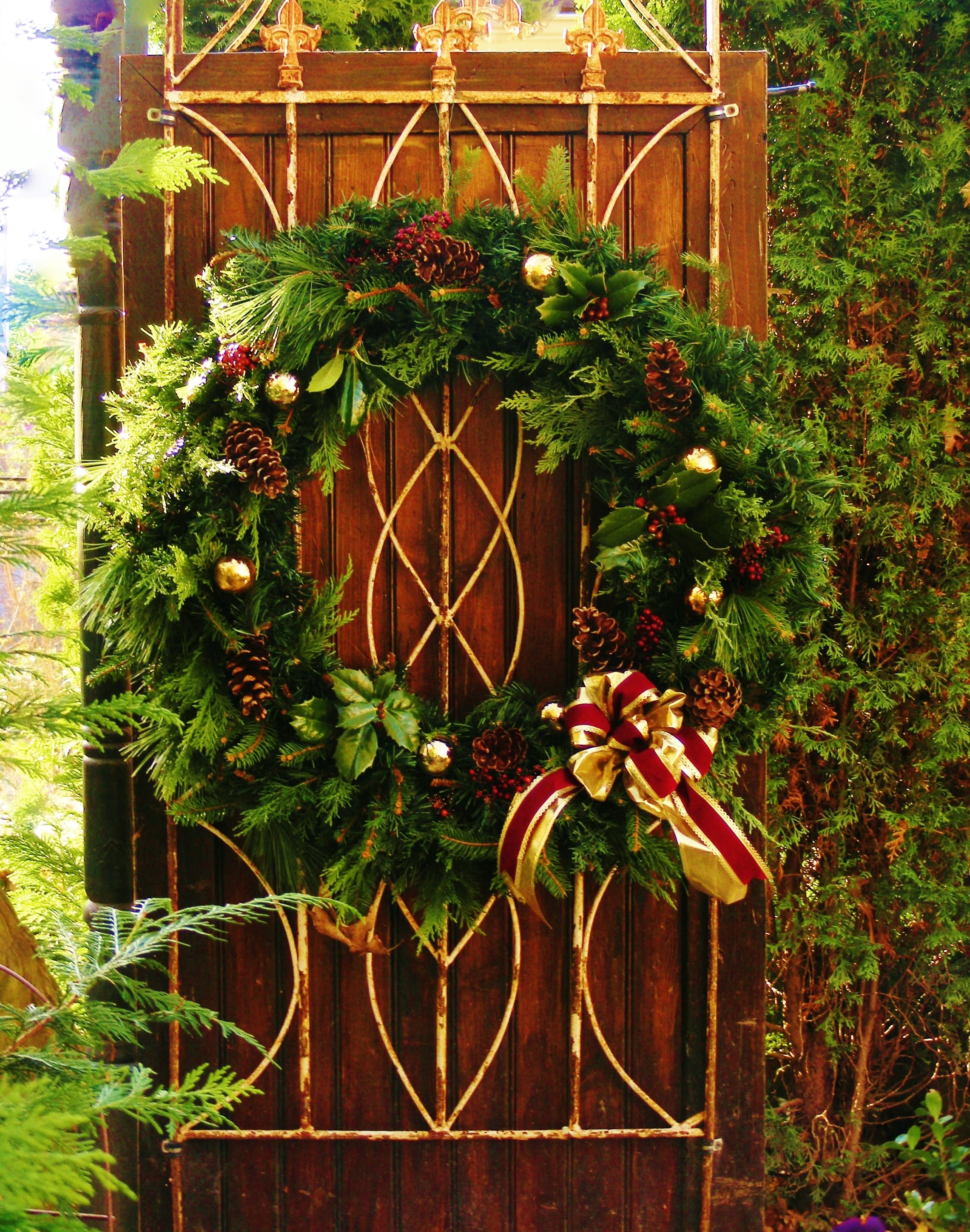Evergreen wreath with pinecones and a red-and-gold bow on a wooden gate