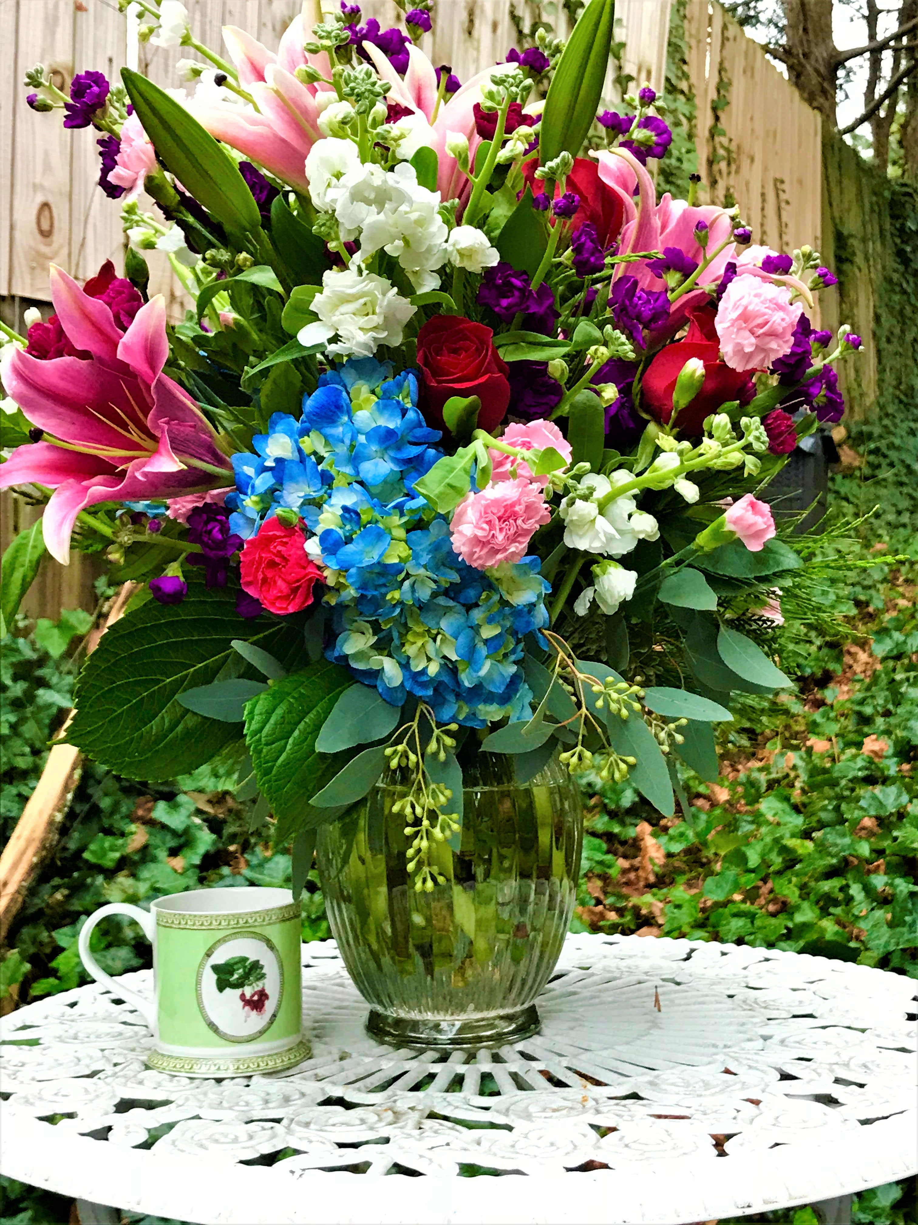 Colorful mixed bouquet in a glass vase with a mug beside it