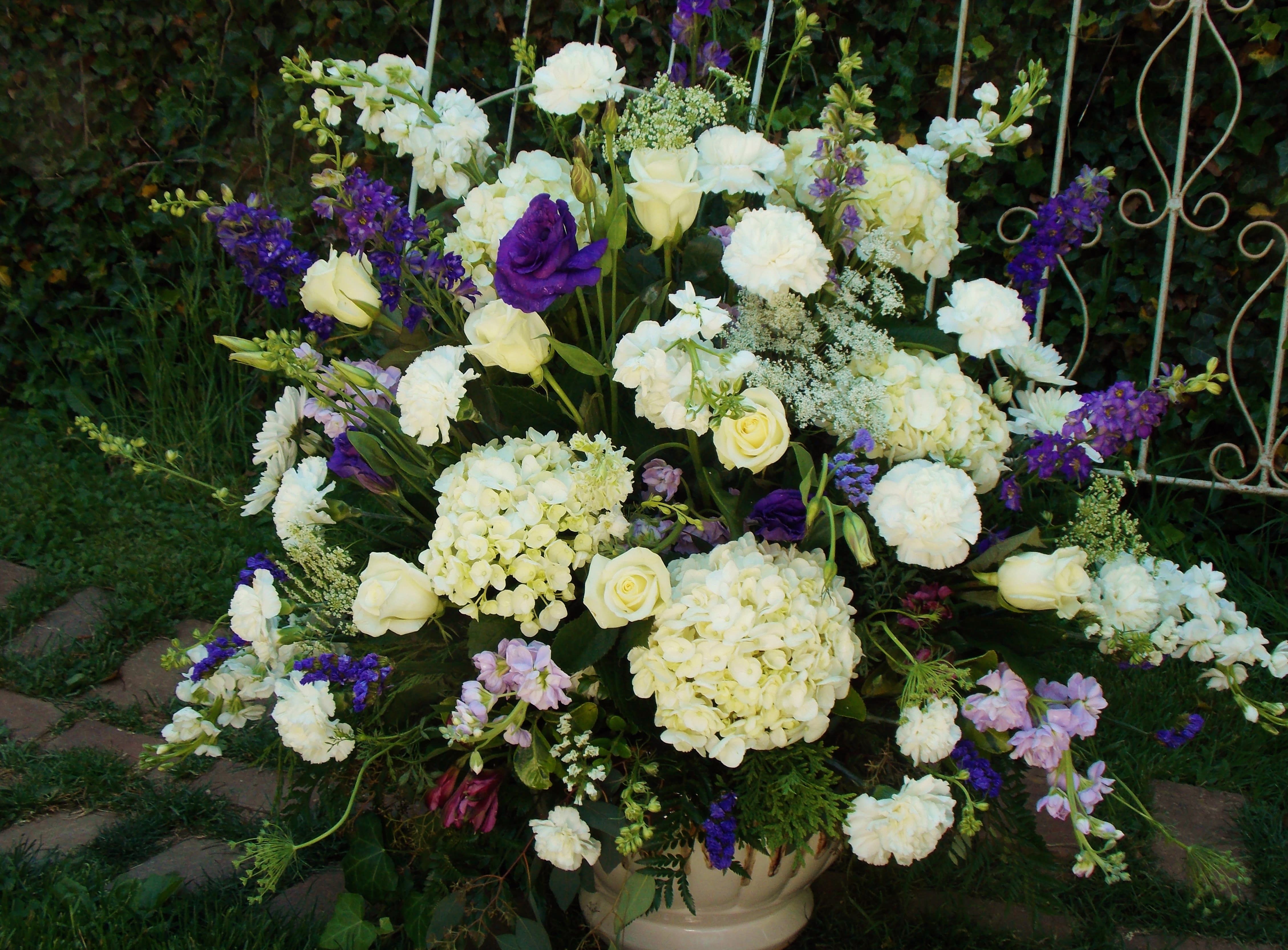 Large white and purple floral arrangement in a cream vase