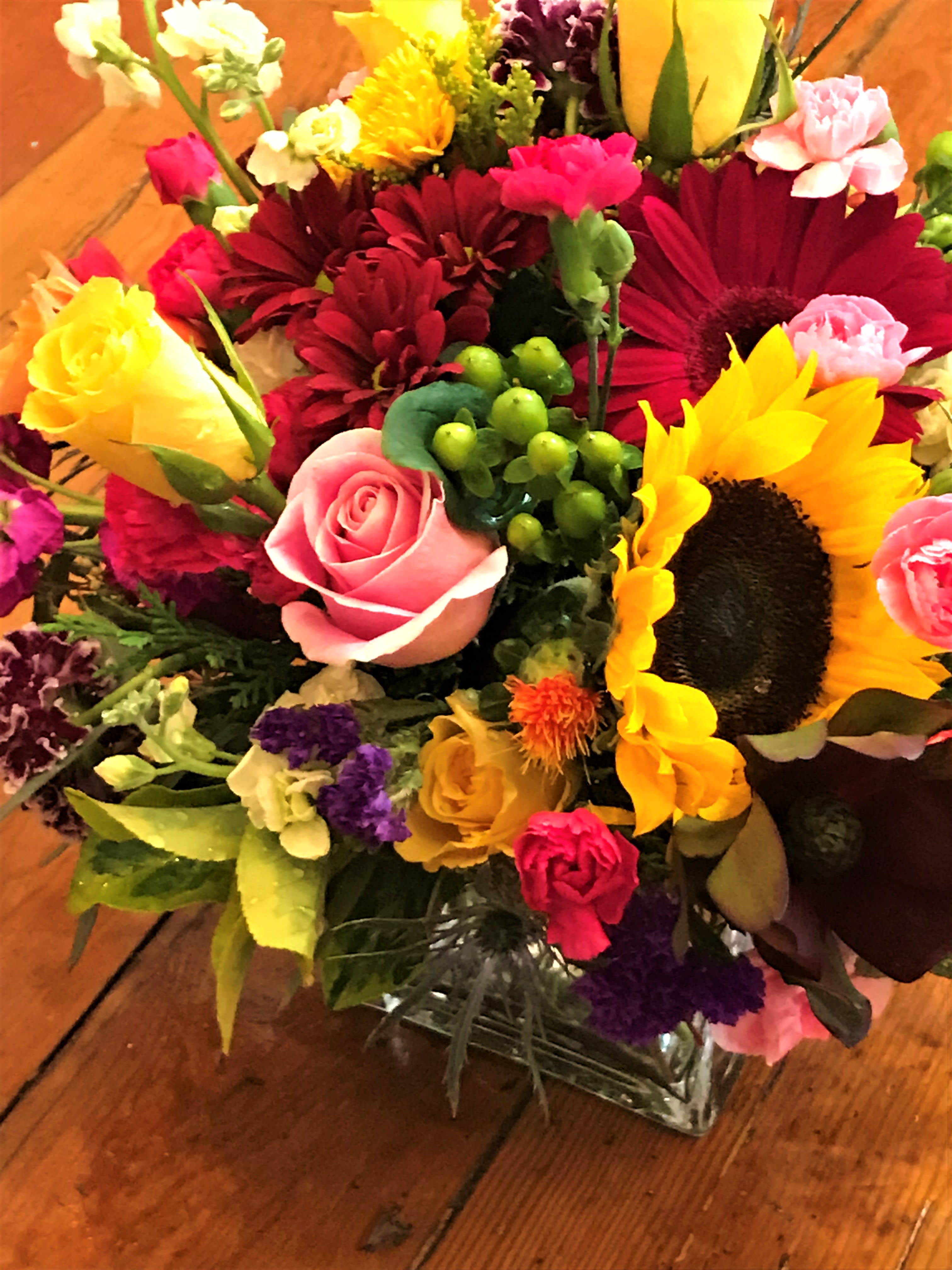 Mixed bouquet with sunflowers, roses, and gerbera daisies in a glass vase