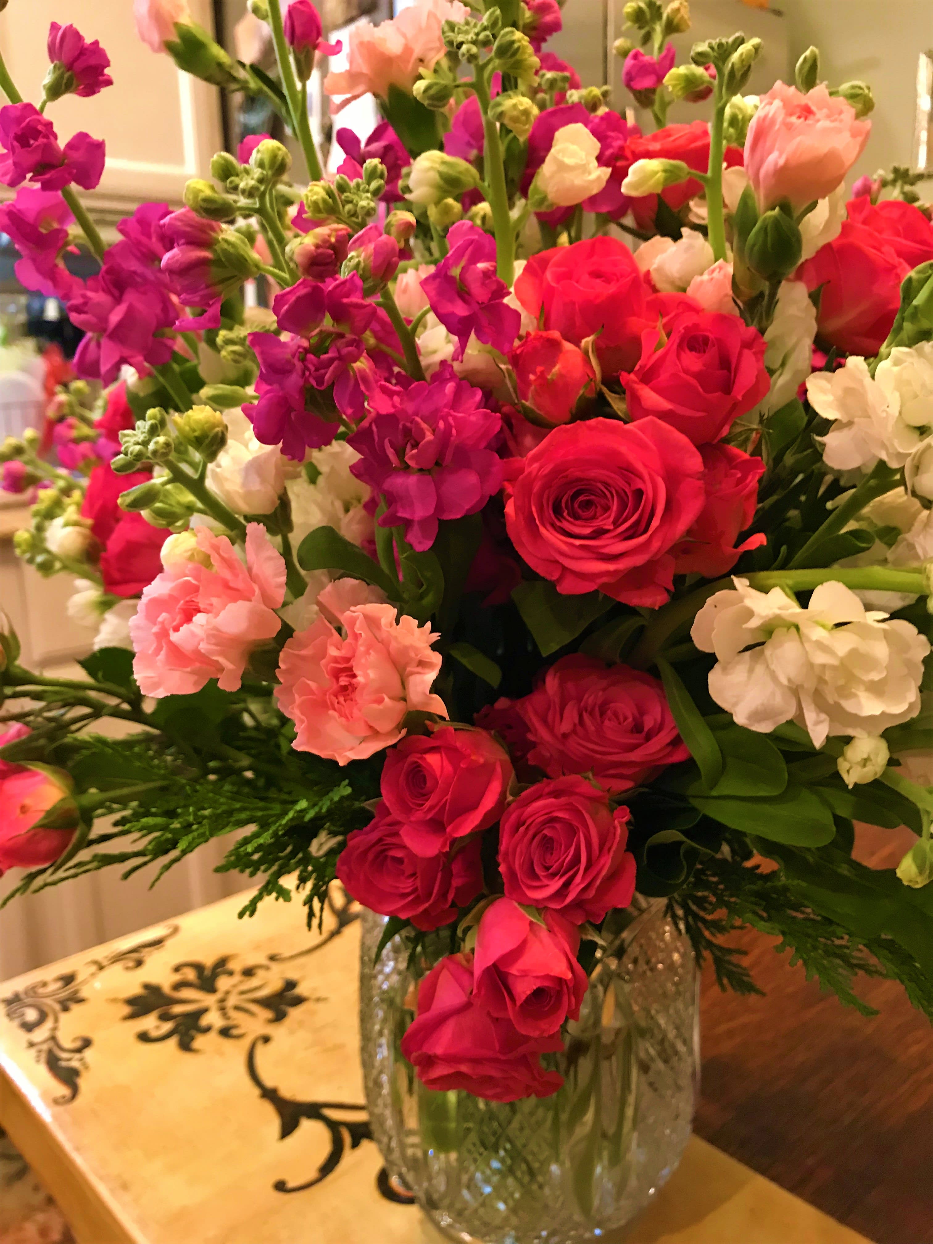 Bouquet of pink roses, carnations, and purple blooms in a glass vase