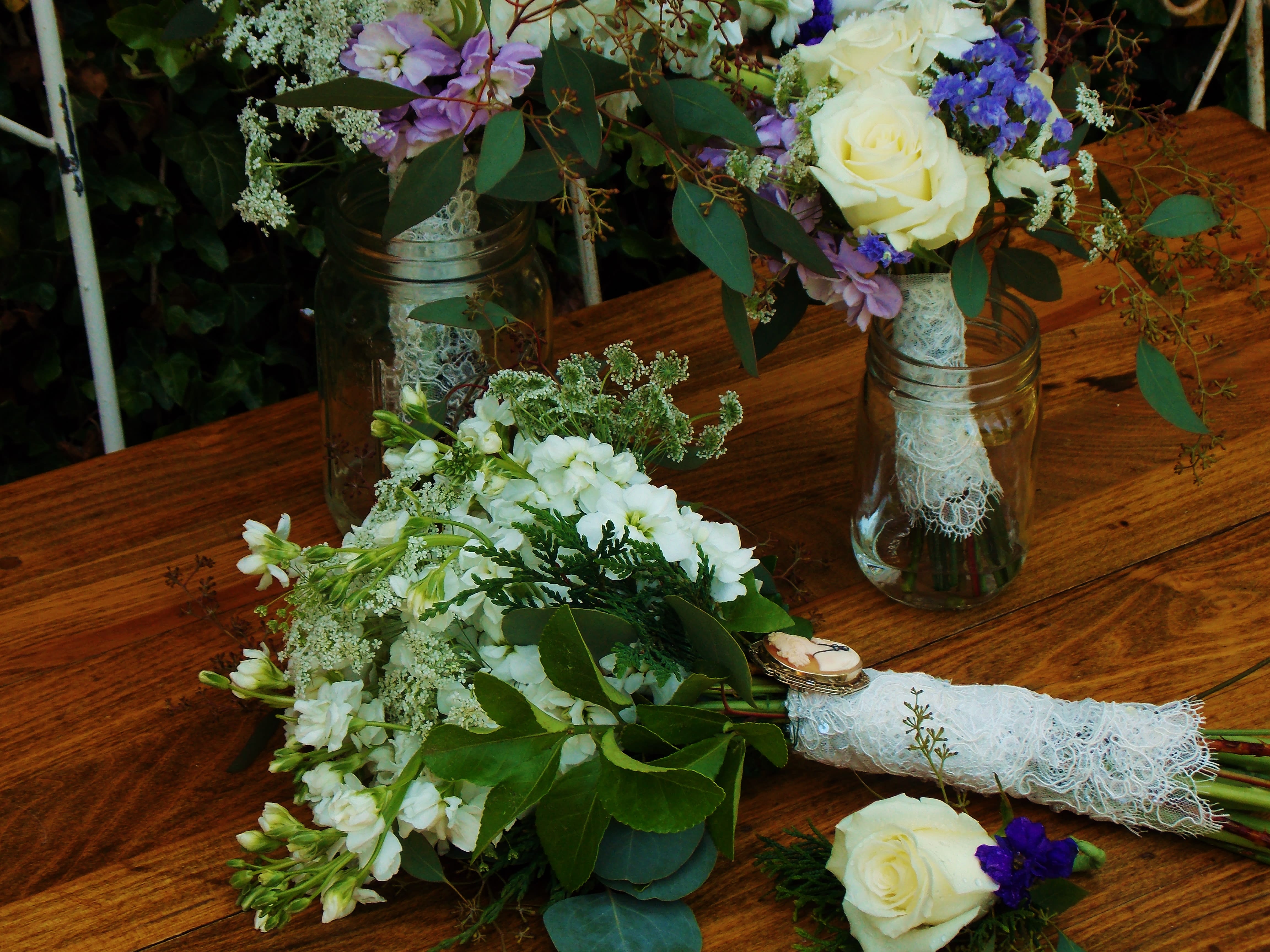 White and purple floral bouquets in glass jars on a wooden table