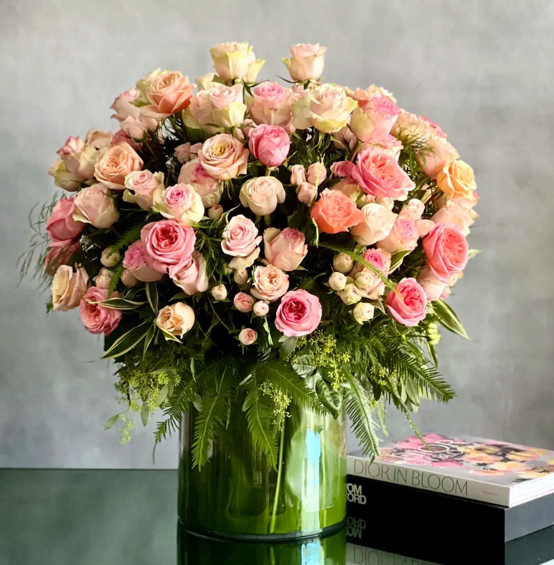Large arrangement of pink and peach roses in a green glass cylinder vase on a table