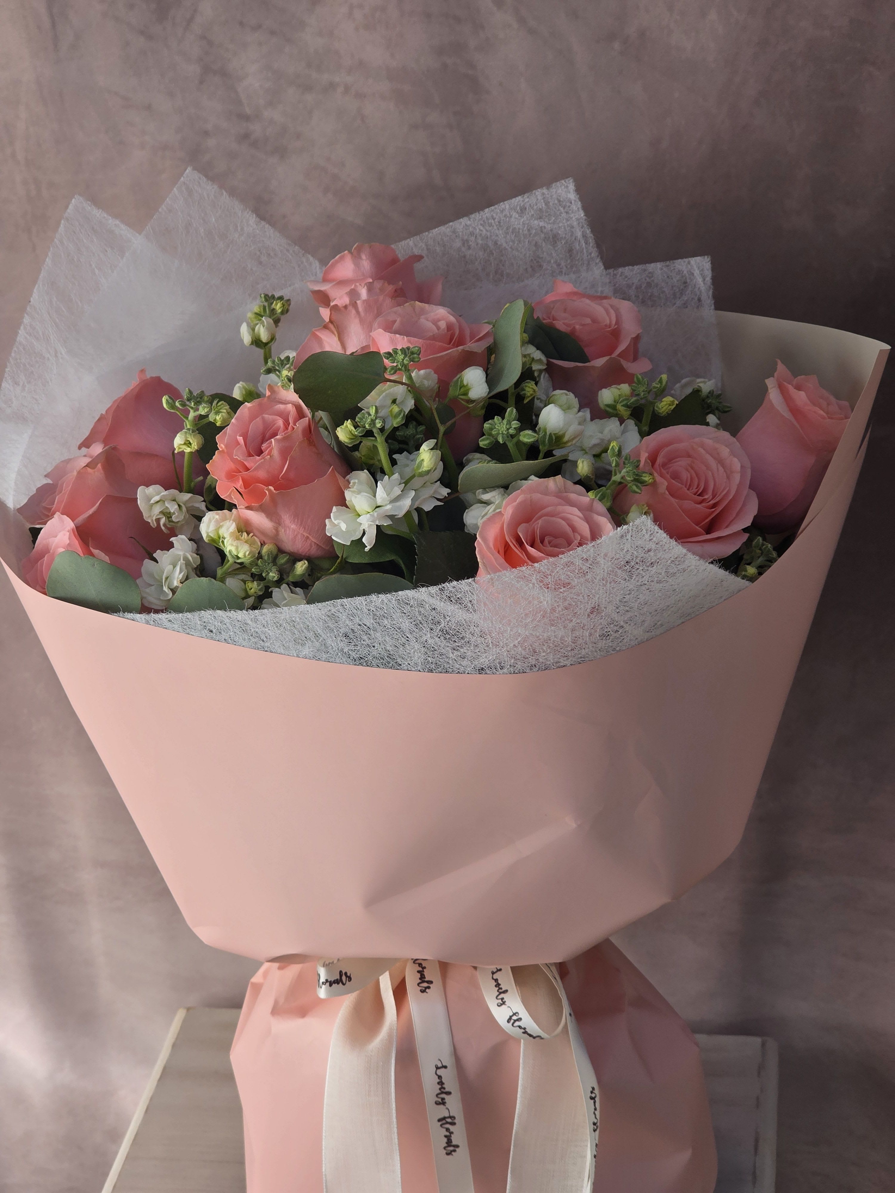 Rosé Petal Charm - A delicate bouquet of blush pink roses paired with soft white blooms and fresh greenery, beautifully wrapped in pastel pink. Elegant, feminine, and full of gentle romance, this arrangement is perfect for making someone feel truly special.