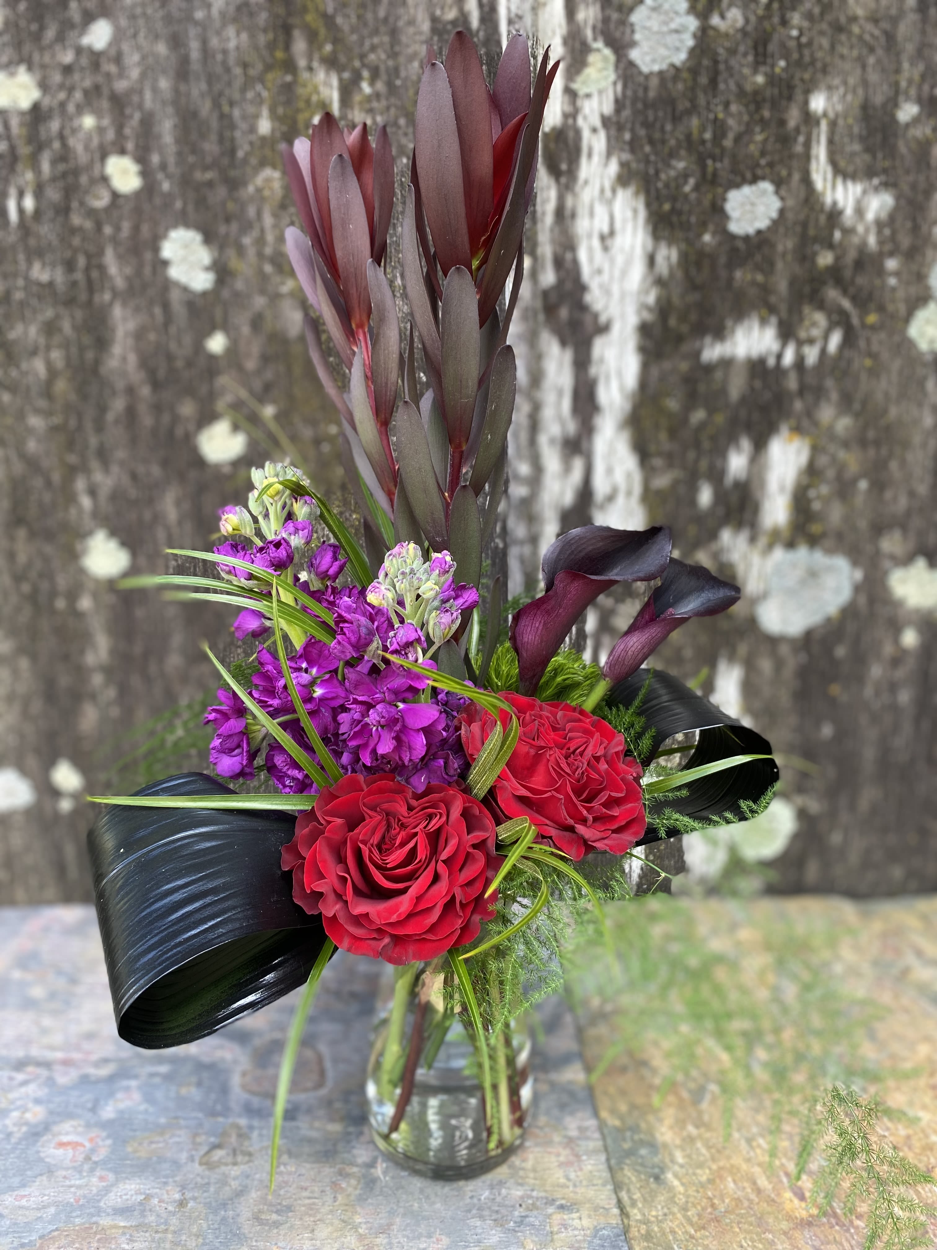 Bouquet of red roses, purple flowers, and dark calla lilies in a glass vase