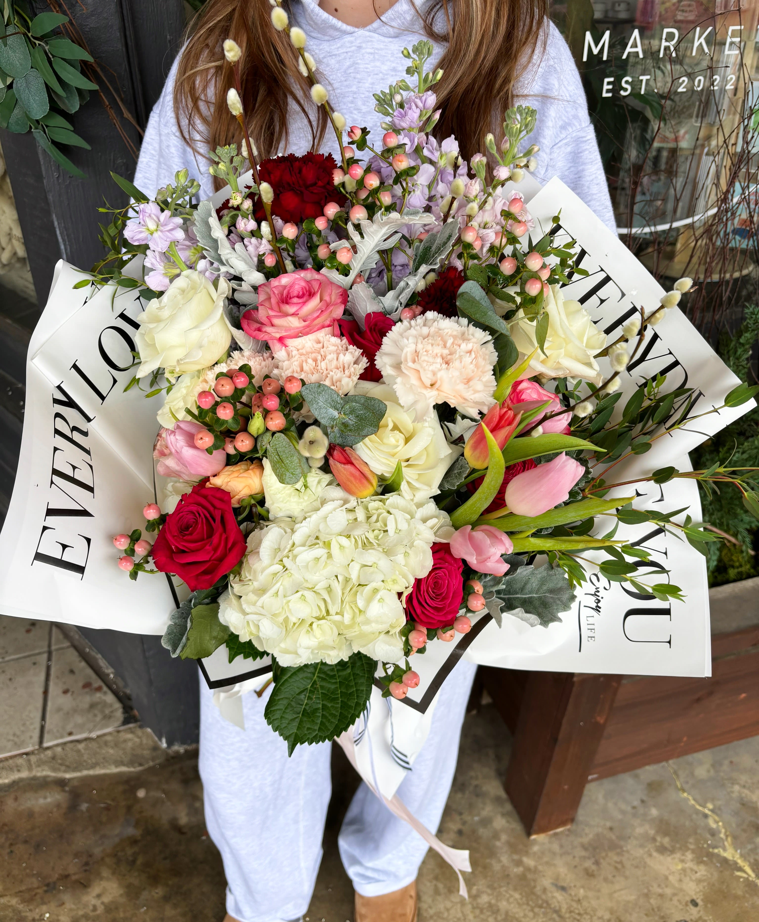 Large bouquet of mixed pink, white, and red flowers wrapped in white paper