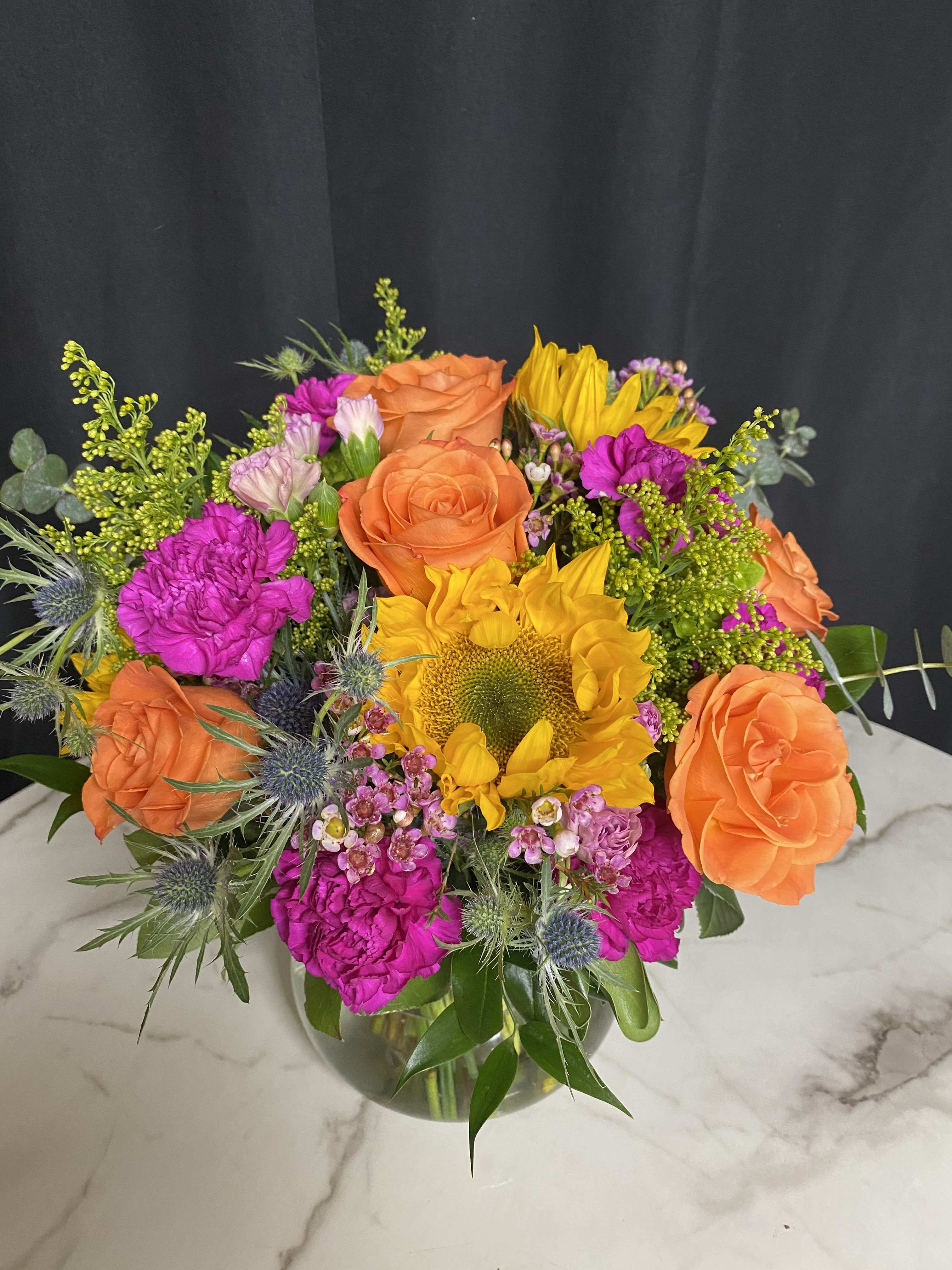 Bouquet of orange roses, yellow sunflower, and bright pink flowers in a glass vase