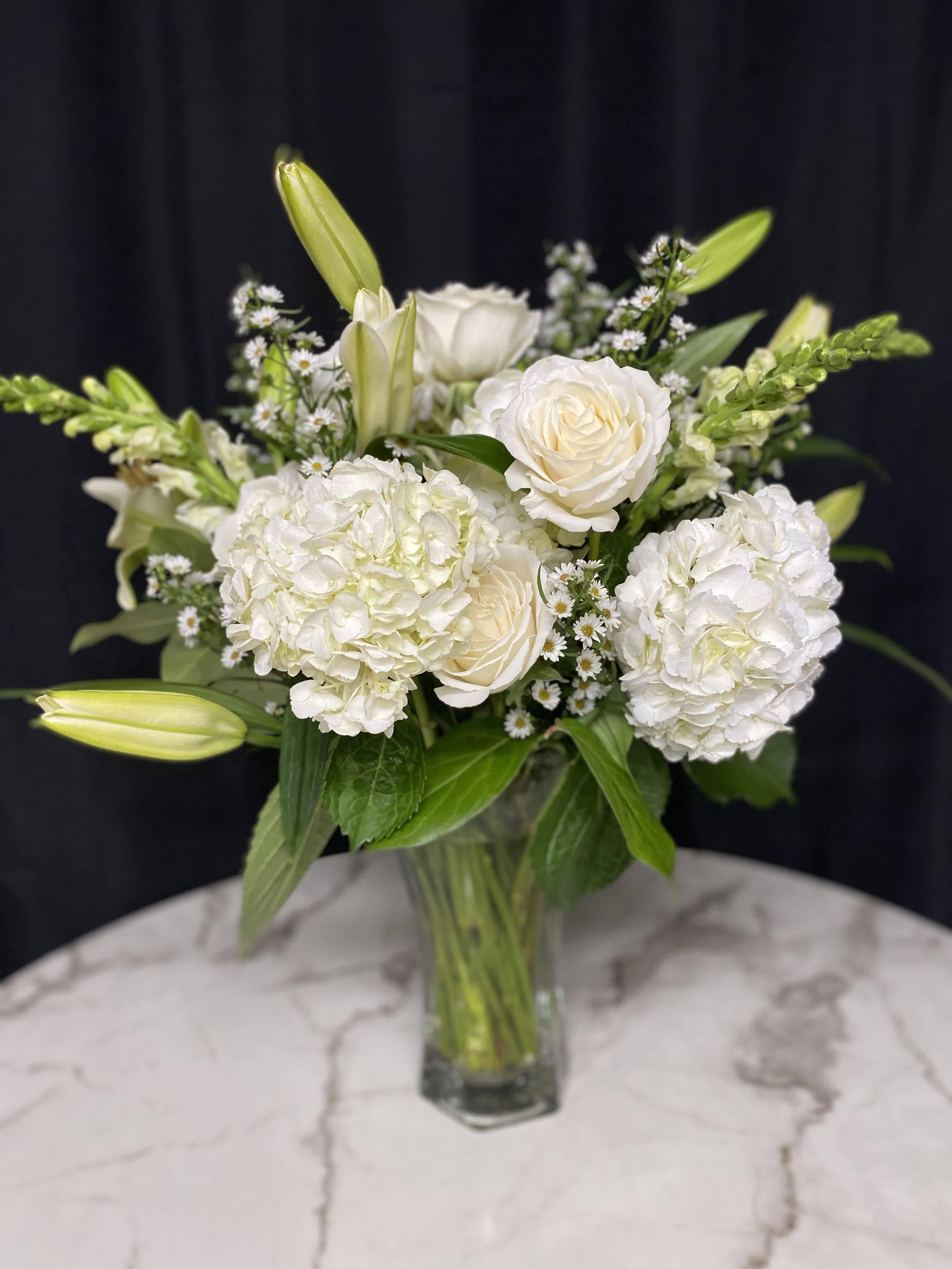 White roses and hydrangeas in a glass vase with lily buds