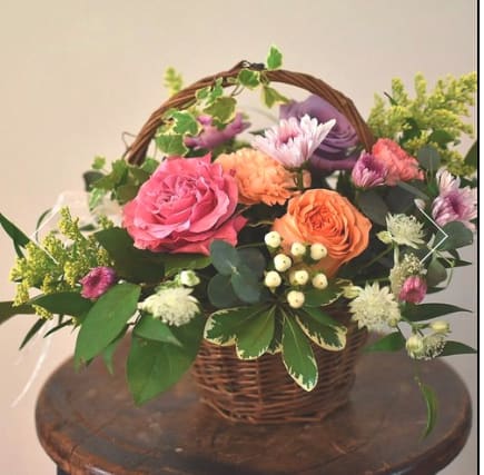 Basket arrangement of pink and orange roses with purple blooms