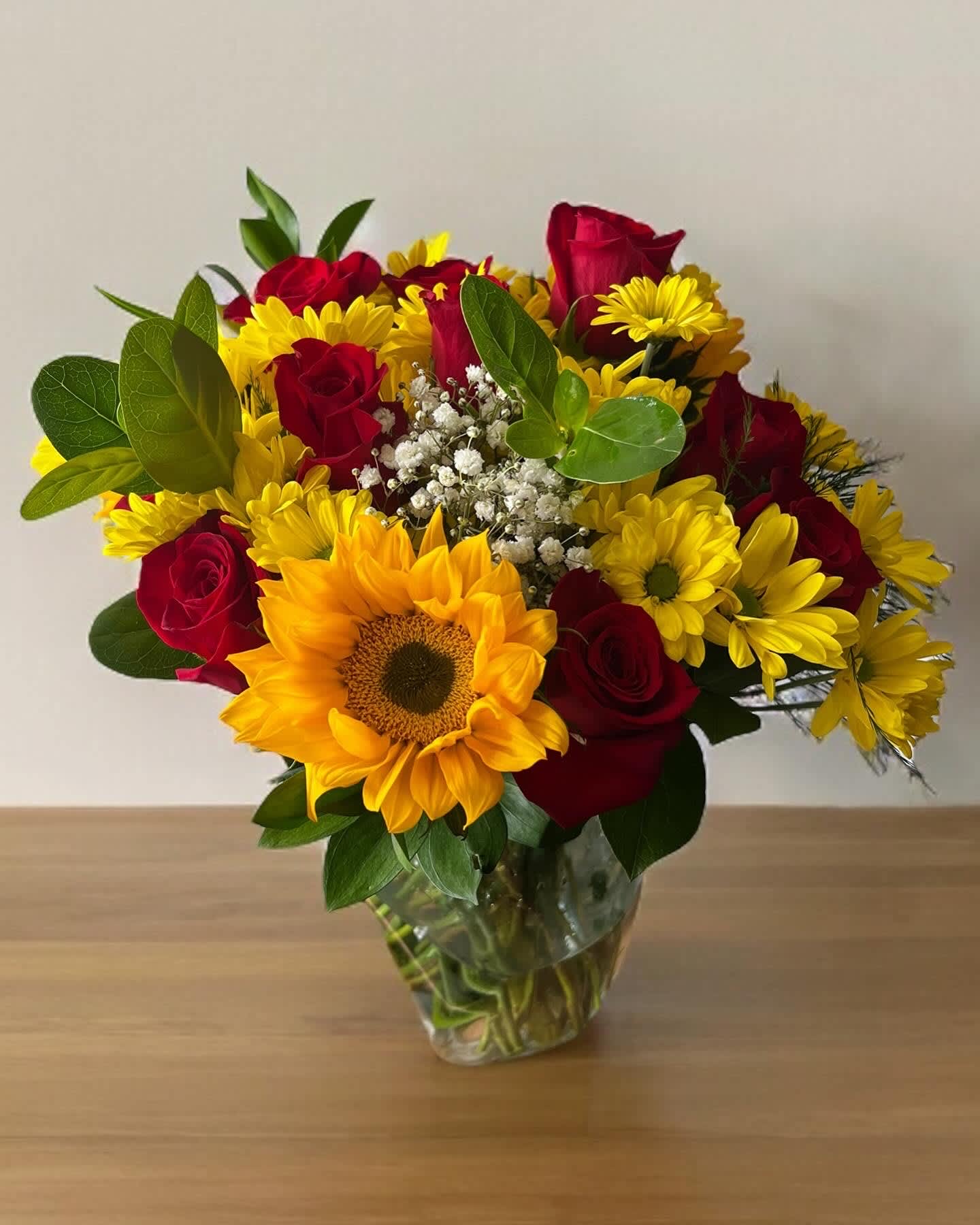 Bouquet of red roses and yellow sunflowers in a clear glass vase