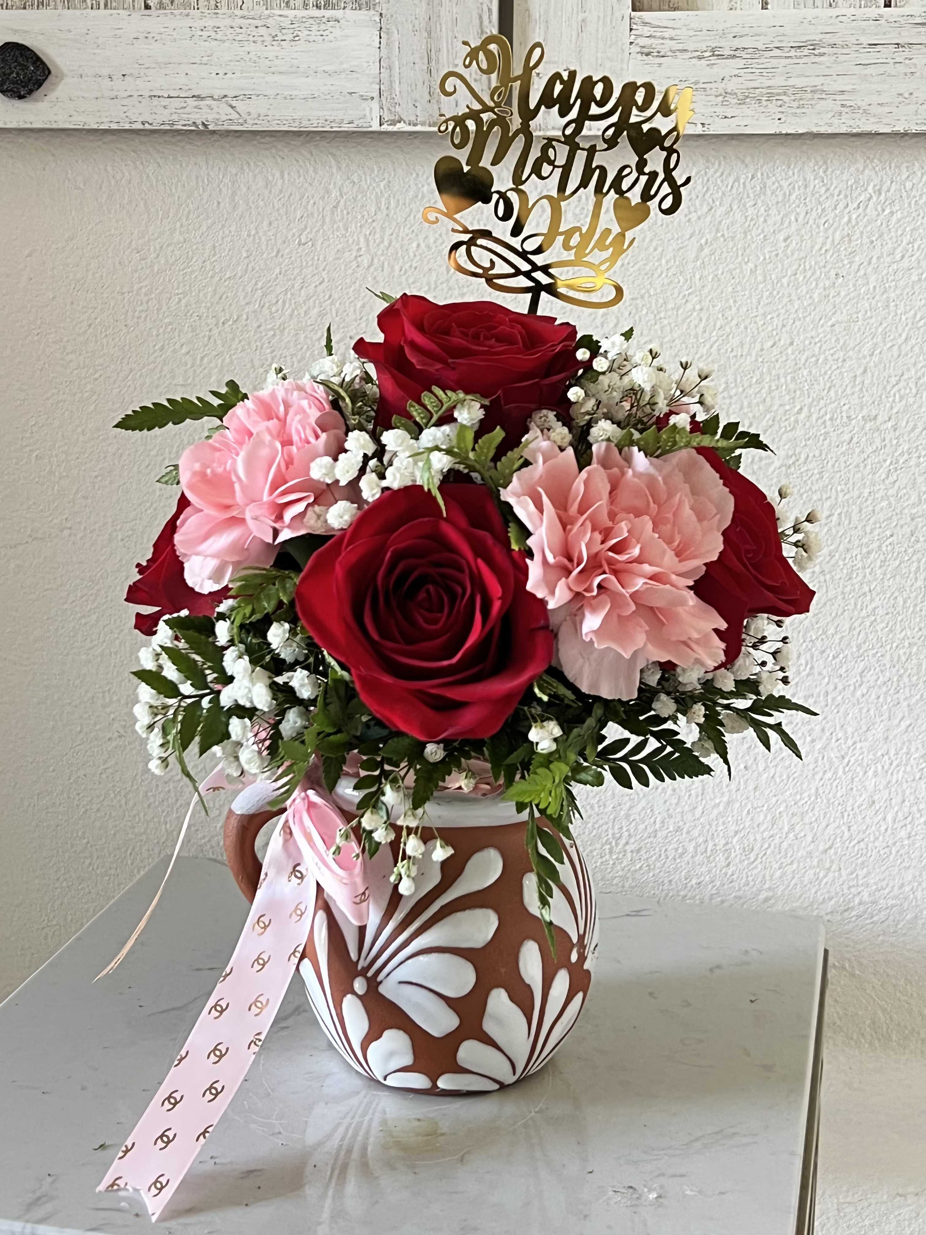 My Mom's Cantarito - Celebrate her with My Mom’s Cantarito, a stunning fusion of cultural heritage and timeless elegance. This handcrafted arrangement is nestled inside a traditional, artisanal clay jar, featuring a lush collection of premium velvet red roses and delicate blushing carnations. Accented with airy sprays of baby’s breath and fresh greenery, this boutique floral design offers a rustic yet sophisticated charm that stands out from standard bouquets. More than just a gift, the authentic terra-cotta vessel serves as a lasting keepsake she can cherish long after the blooms have faded. Give her a piece of tradition and a burst of beauty that says "Happy Mother’s Day" with true heart and style.