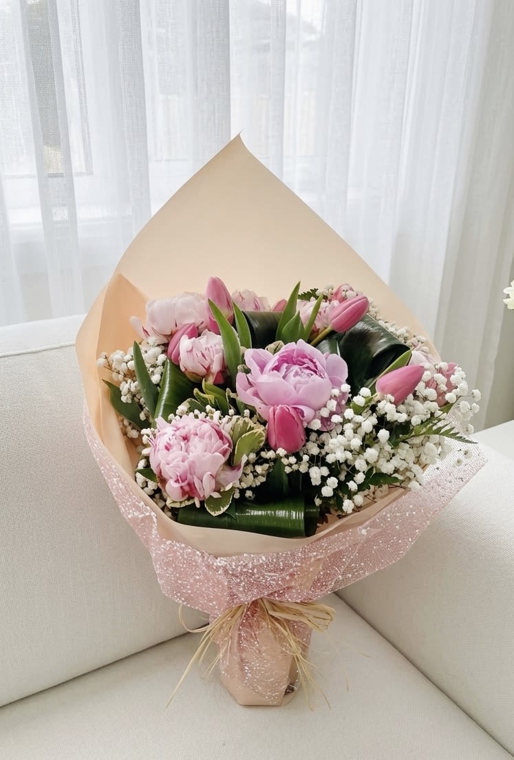 Peony &amp; Tulip Splendor - Sparkling Pink Bouquet - A luxurious and feminine spring bouquet featuring lush pink peonies and vibrant pink tulips. This elegant arrangement is filled with delicate white baby's breath and structured green foliage, wrapped in layers of apricot-toned paper and a sparkling pink mesh overlay, finished with a natural raffia bow.