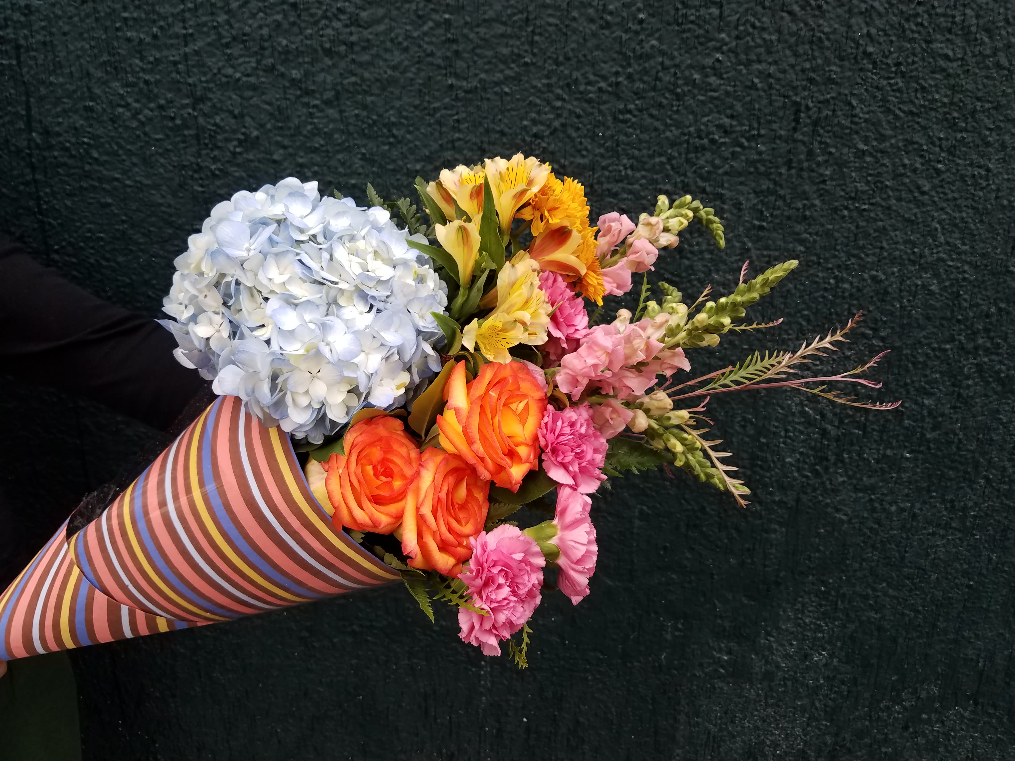 Mixed bouquet with blue hydrangea, orange roses, and pink flowers in striped wrap