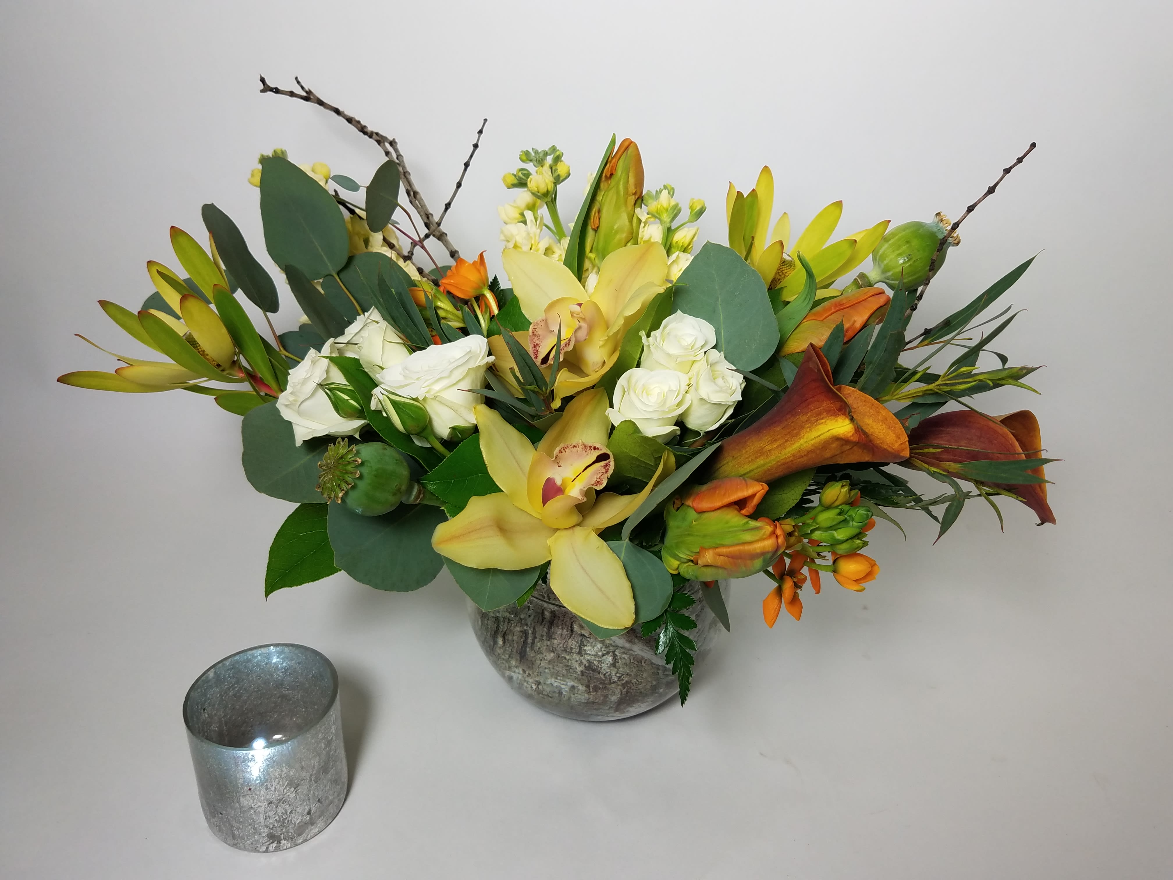 Mixed floral arrangement with yellow orchids, white roses, and orange callas in a vase