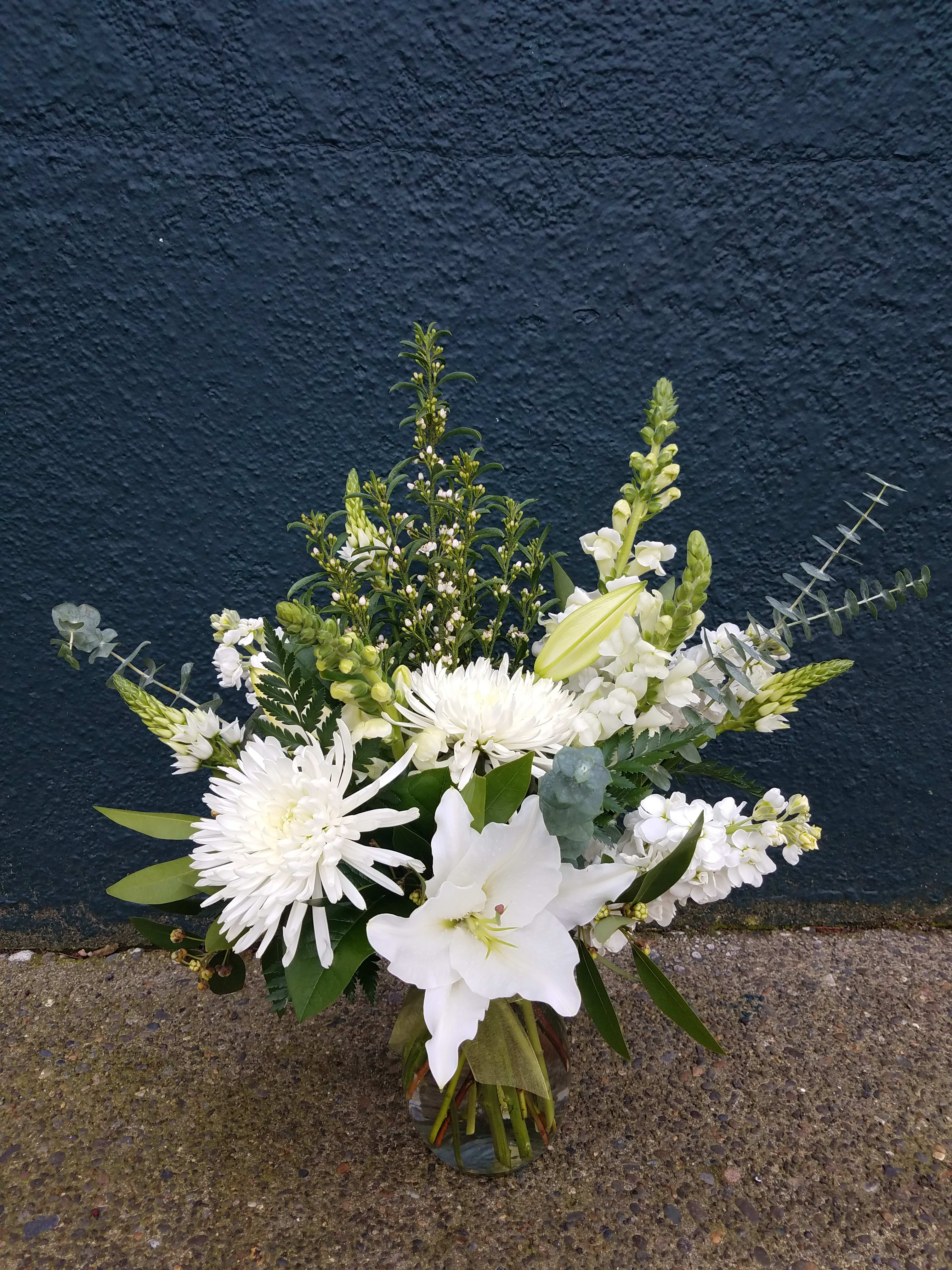 White floral arrangement in a glass vase with lilies and chrysanthemums
