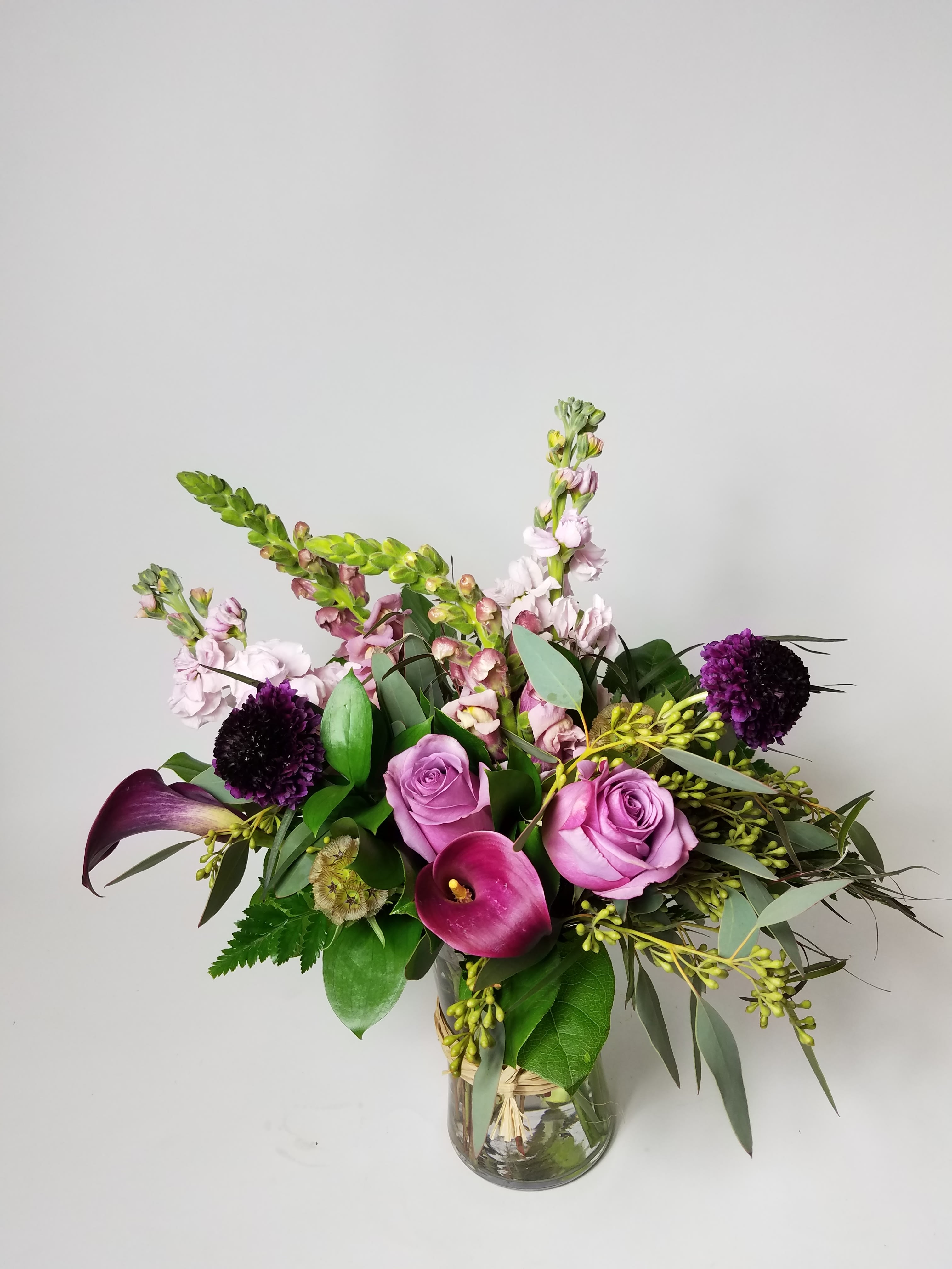 Pink roses and calla lilies in a glass vase with purple blooms