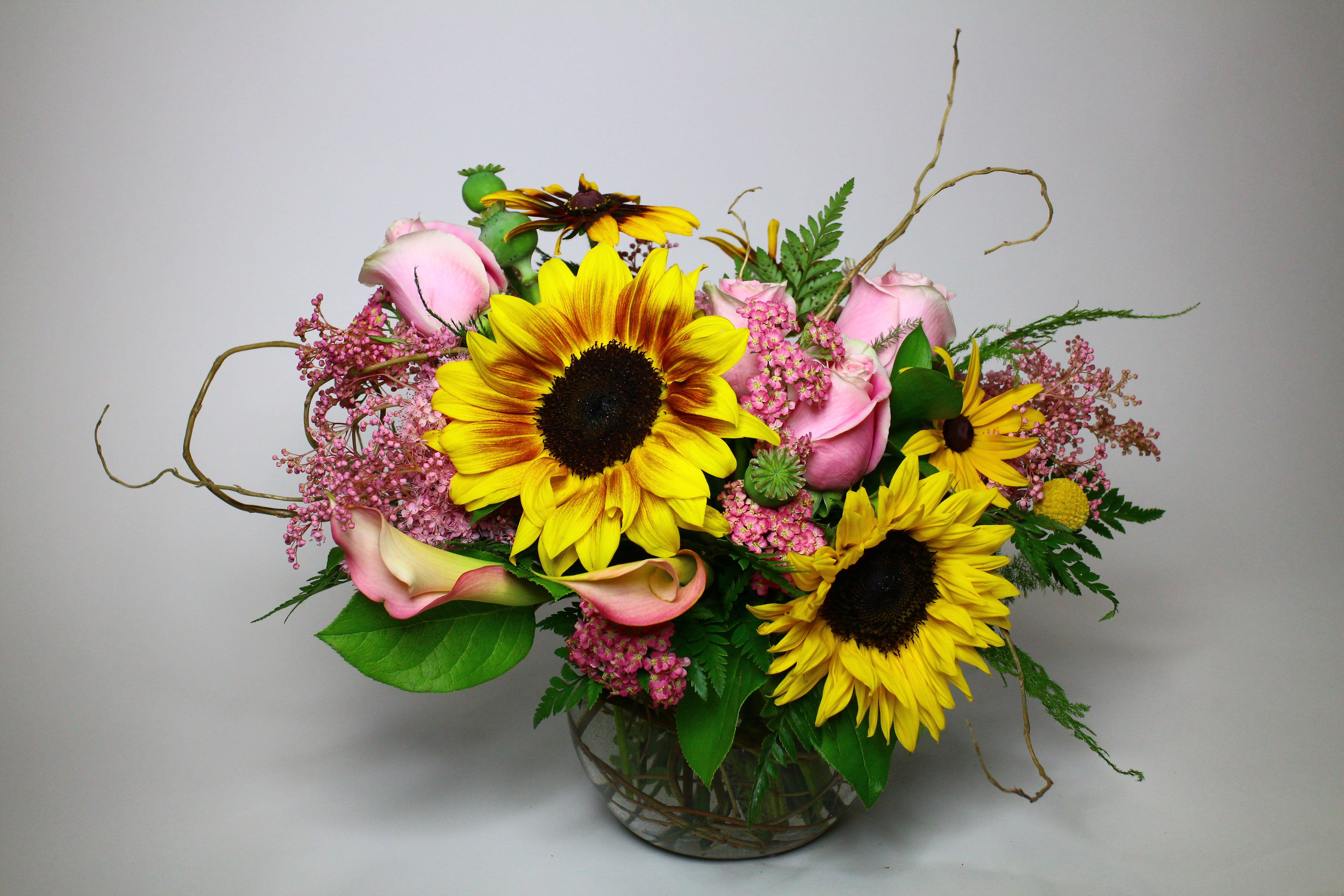 Bouquet of sunflowers, pink roses, and calla lilies in a glass vase
