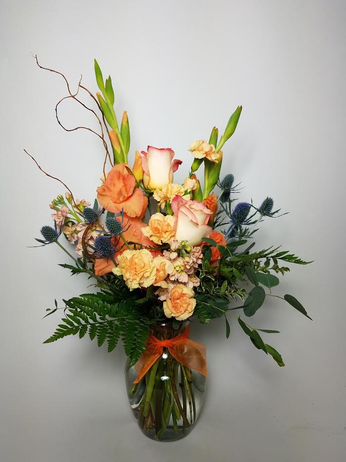 Orange and cream floral arrangement in a glass vase with a ribbon
