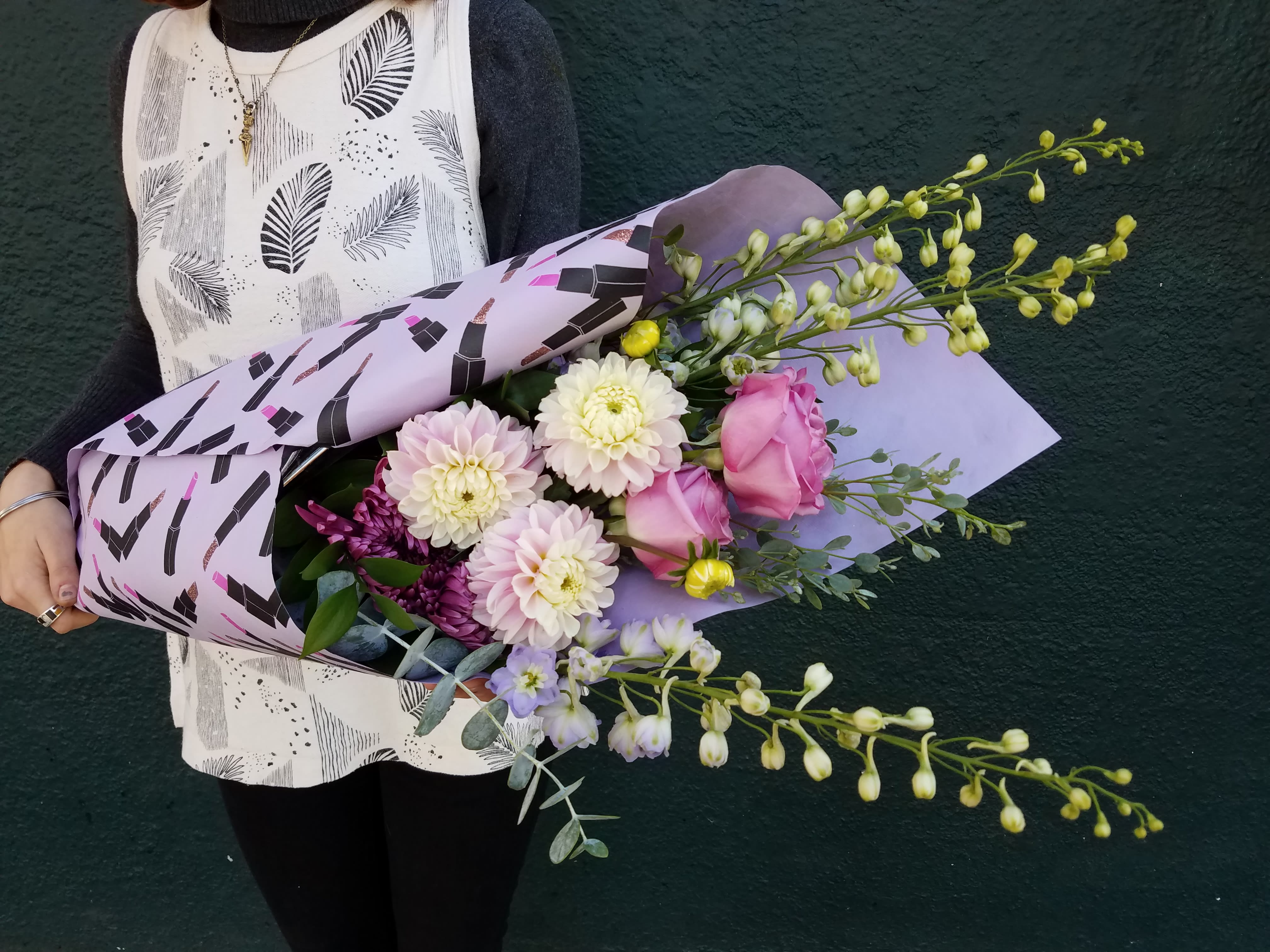 Handheld bouquet of pink and white flowers wrapped in lavender paper