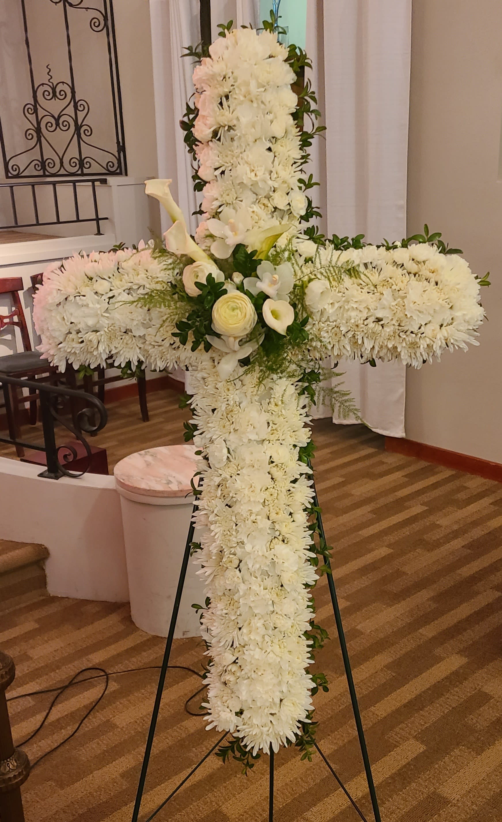 White floral cross on a stand with calla lilies and chrysanthemums