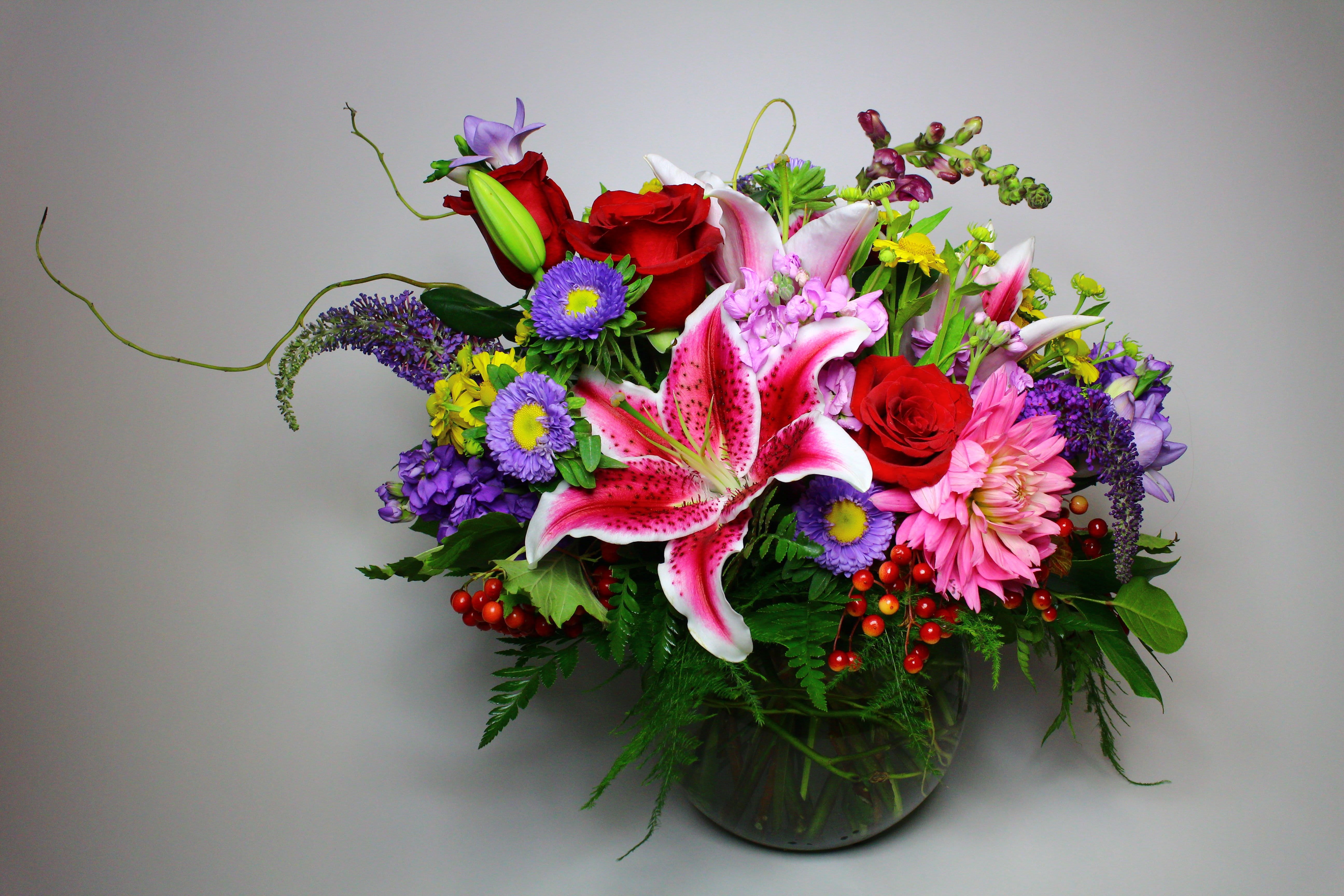 Colorful mixed bouquet with lilies, roses, and daisies in a glass vase