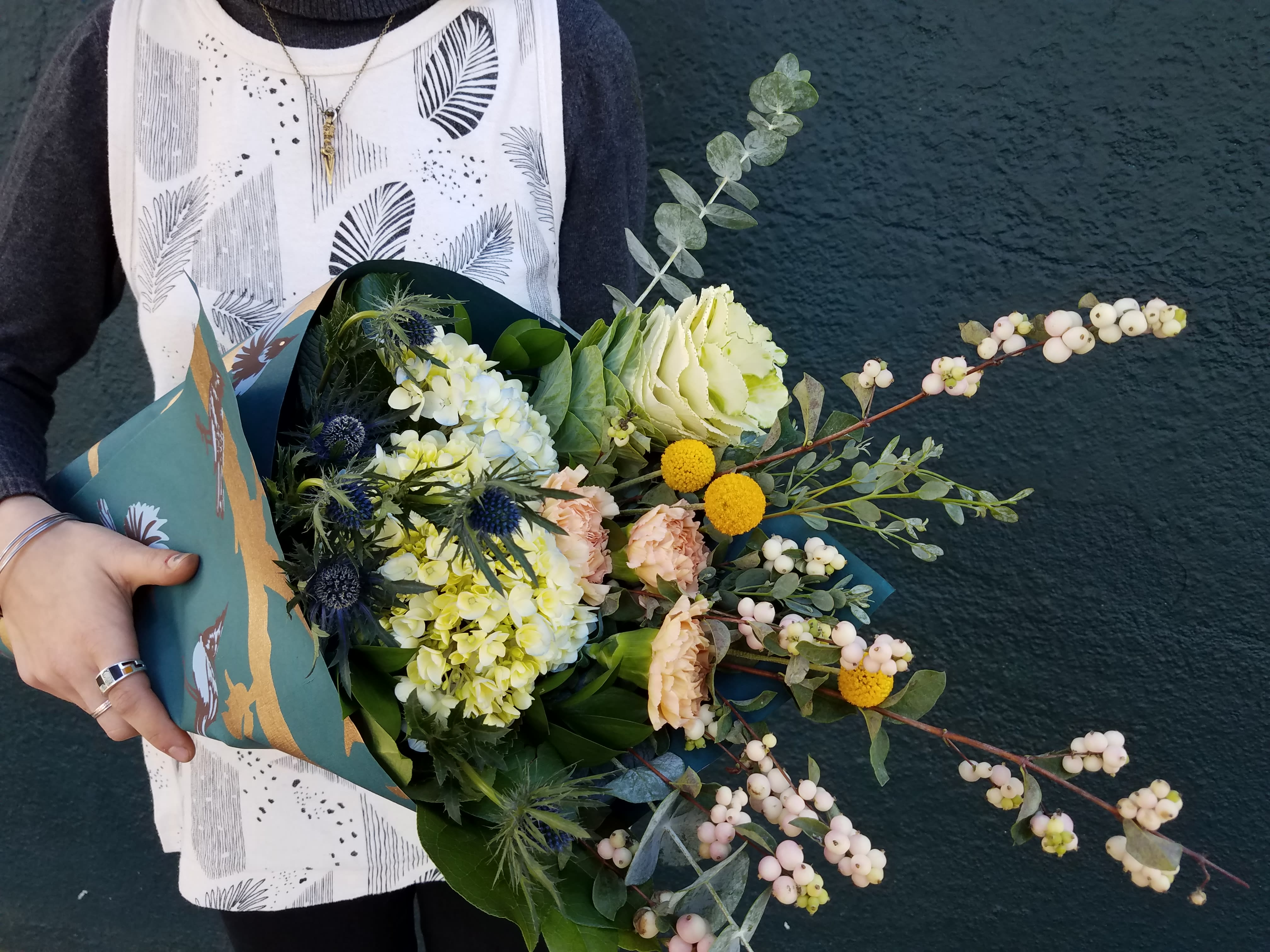 Handheld bouquet with pale flowers and white berries in teal wrapping